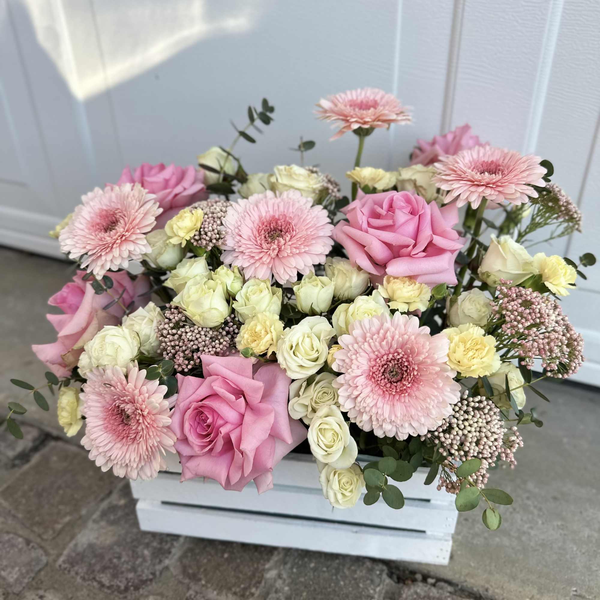 Pink and cream roses with pale pink daisies in a white crate