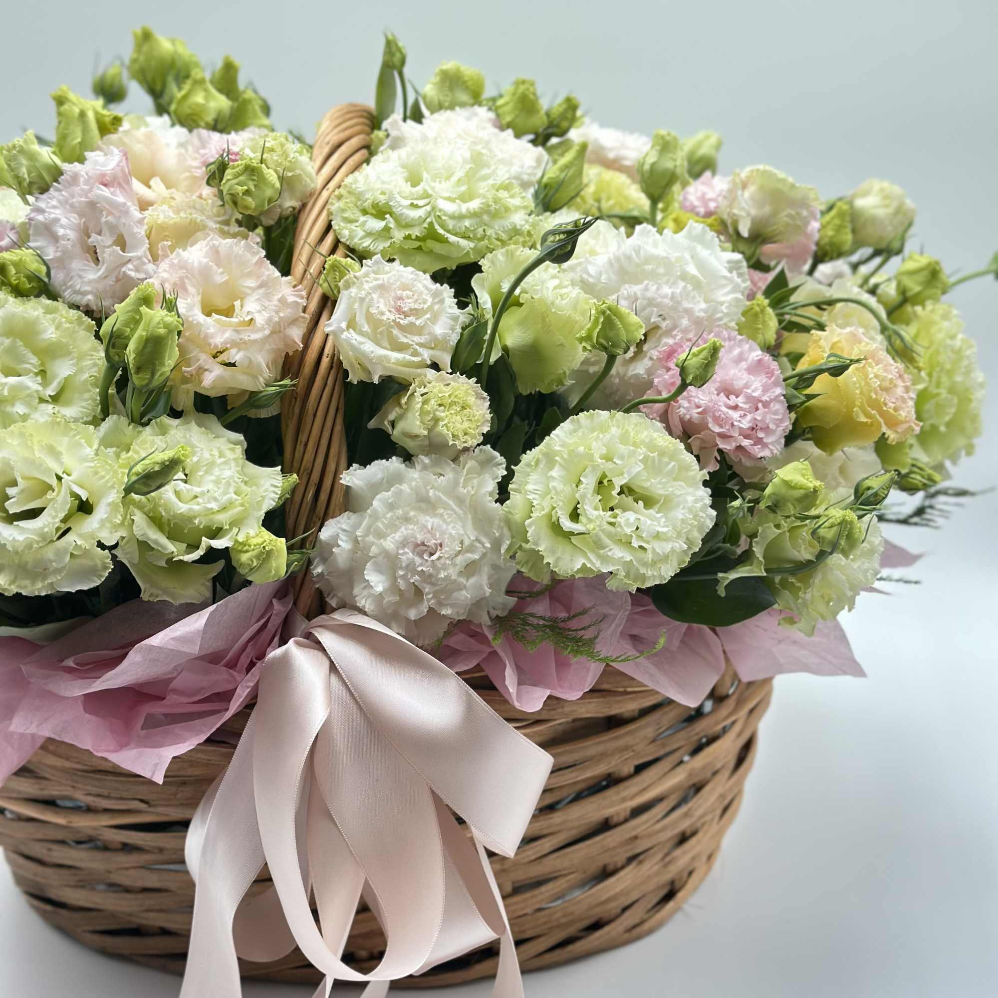 Basket of pale green and white carnations with a pink ribbon