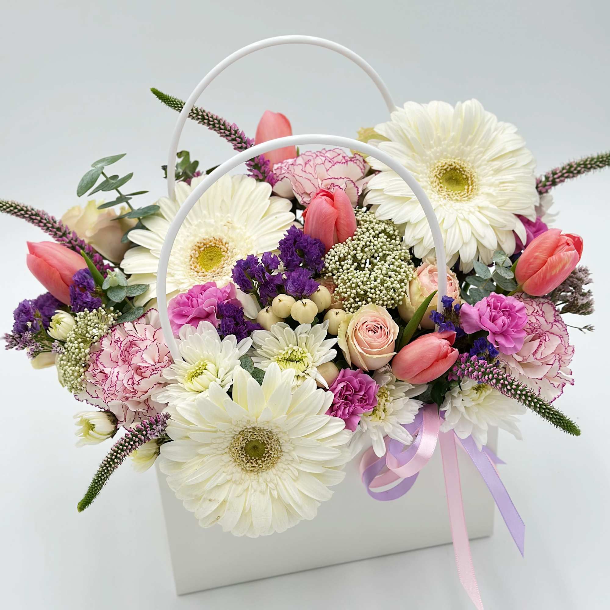 Basket arrangement of white daisies, pink tulips, and purple flowers with ribbon