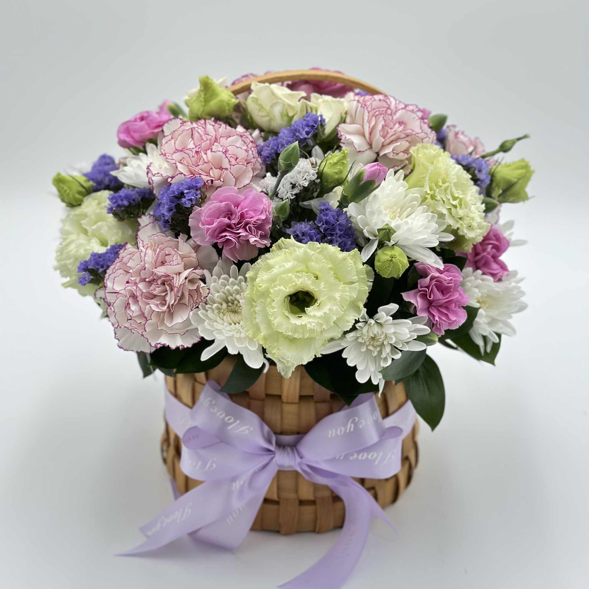 Mixed pink, white, purple, and green flowers in a woven basket with a lavender ribbon