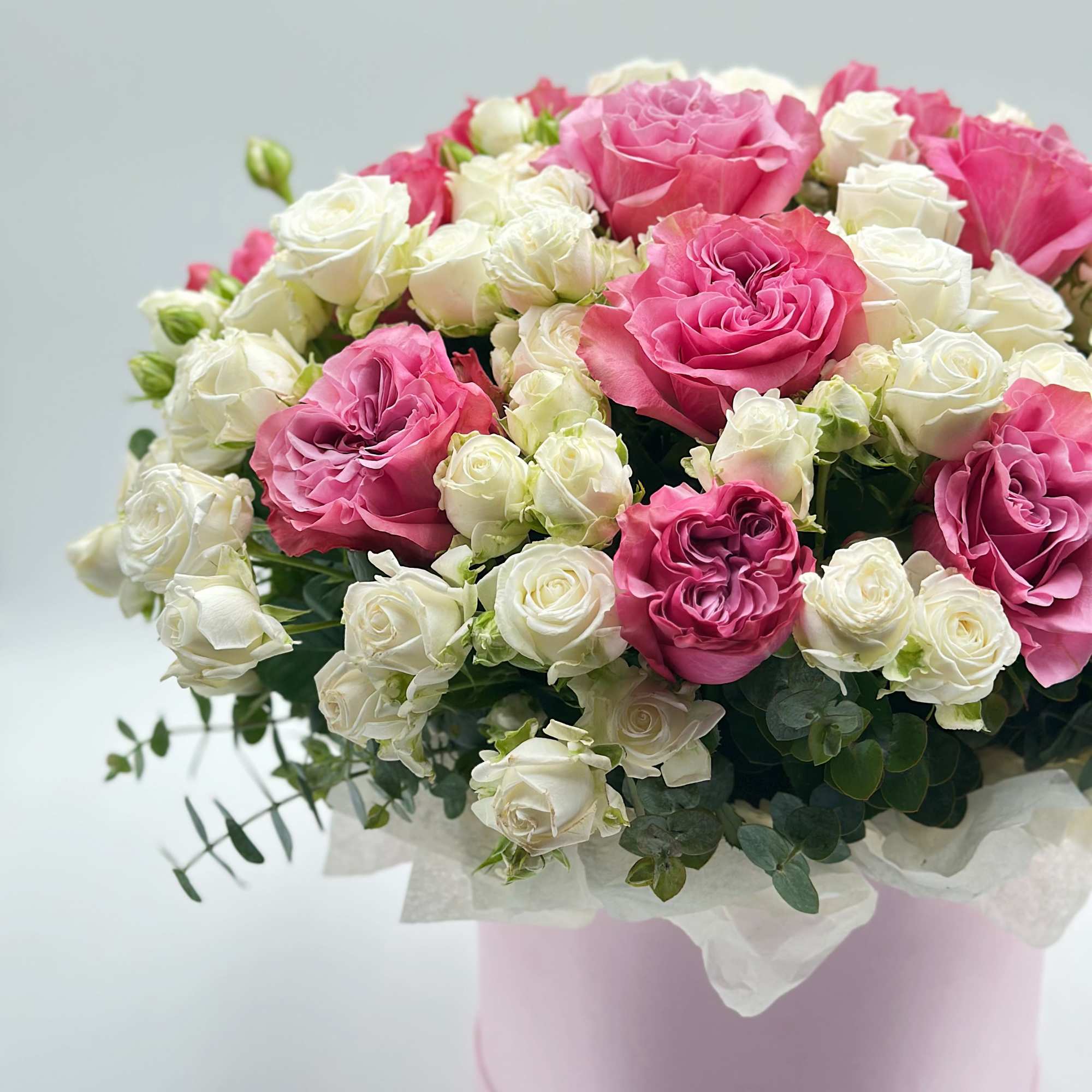 Pink and white roses arranged in a round pastel box