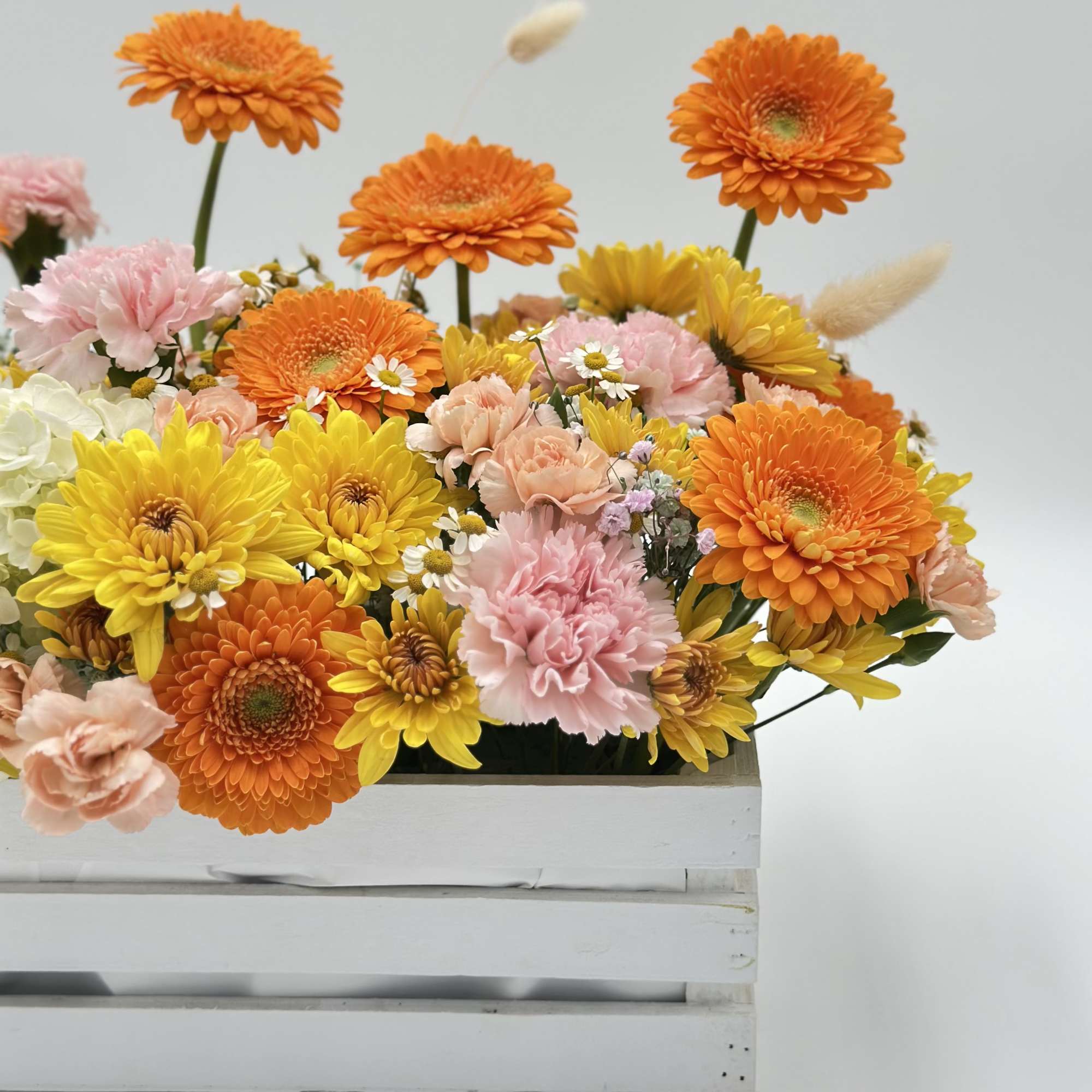 Mixed bouquet of orange, yellow, and pink flowers in a white crate