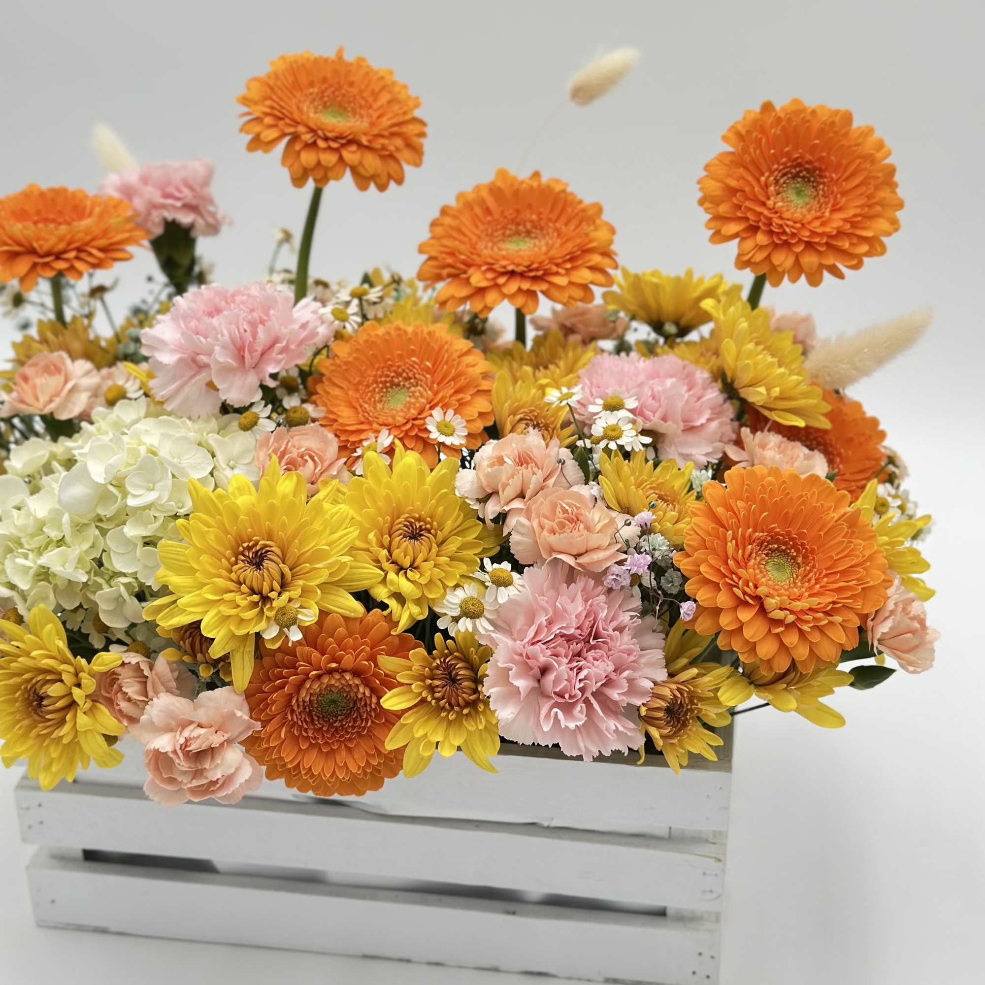 Bright mixed bouquet in a white wooden crate with orange and yellow blooms