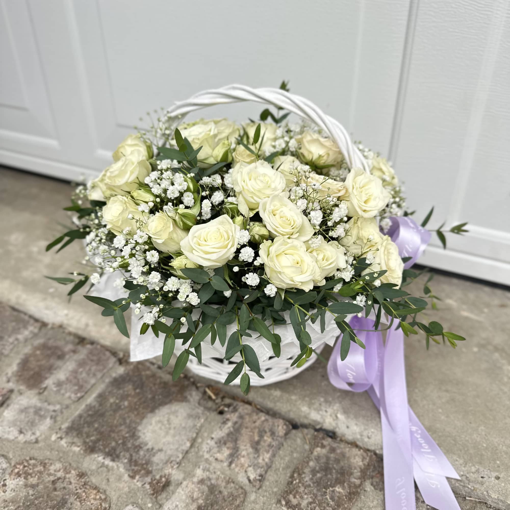 White rose basket arrangement with baby’s breath and a lavender ribbon