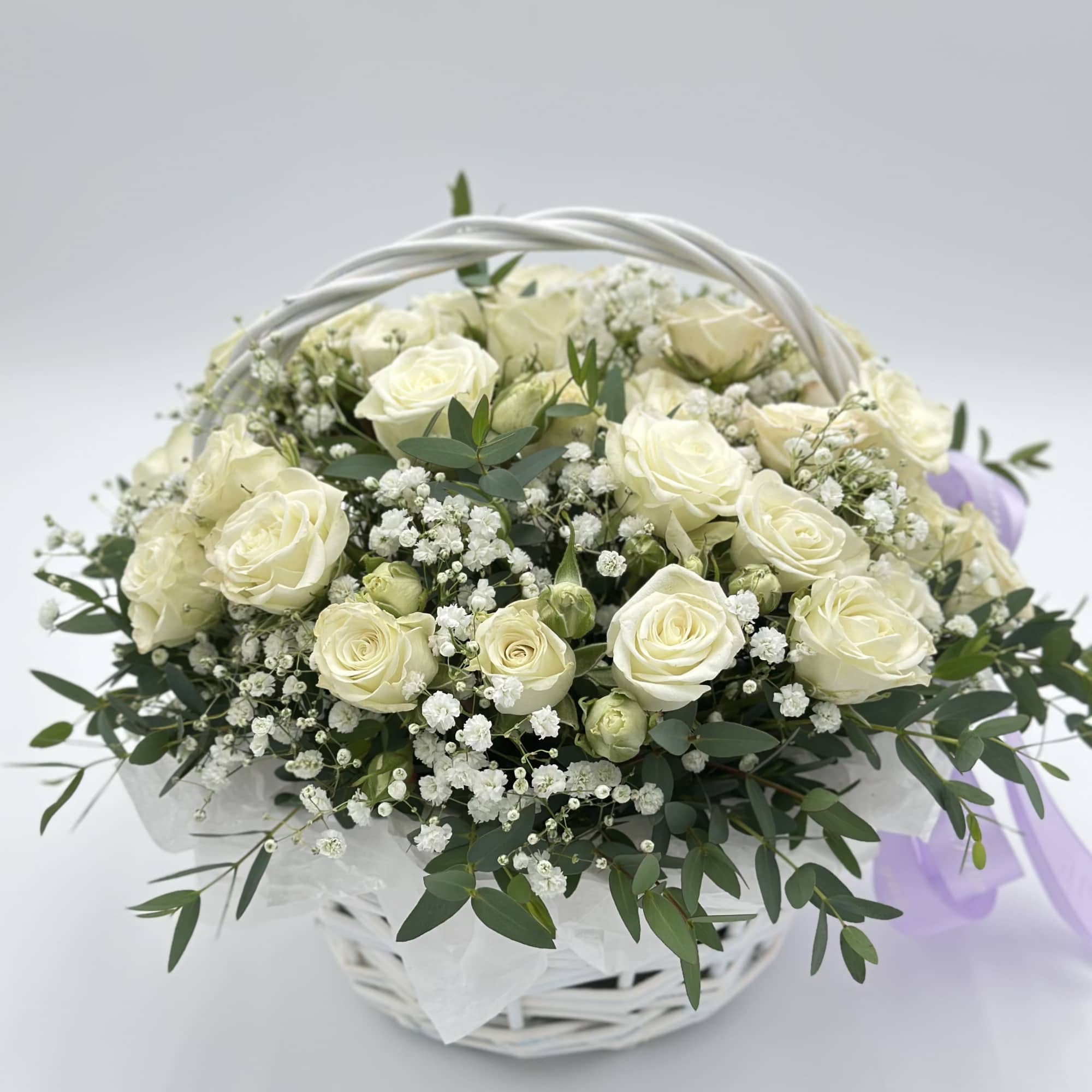 White roses and baby's breath in a white basket with a lavender ribbon