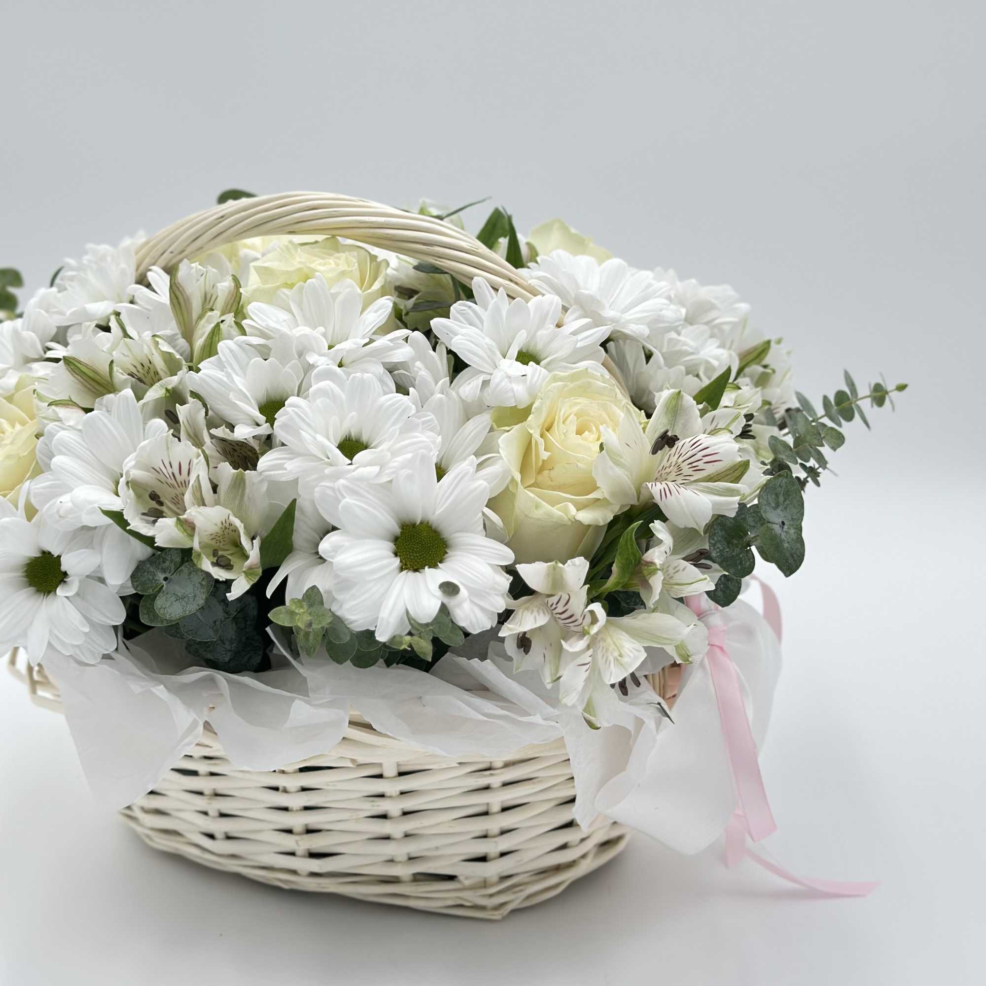 White flowers arranged in a wicker basket with a pink ribbon
