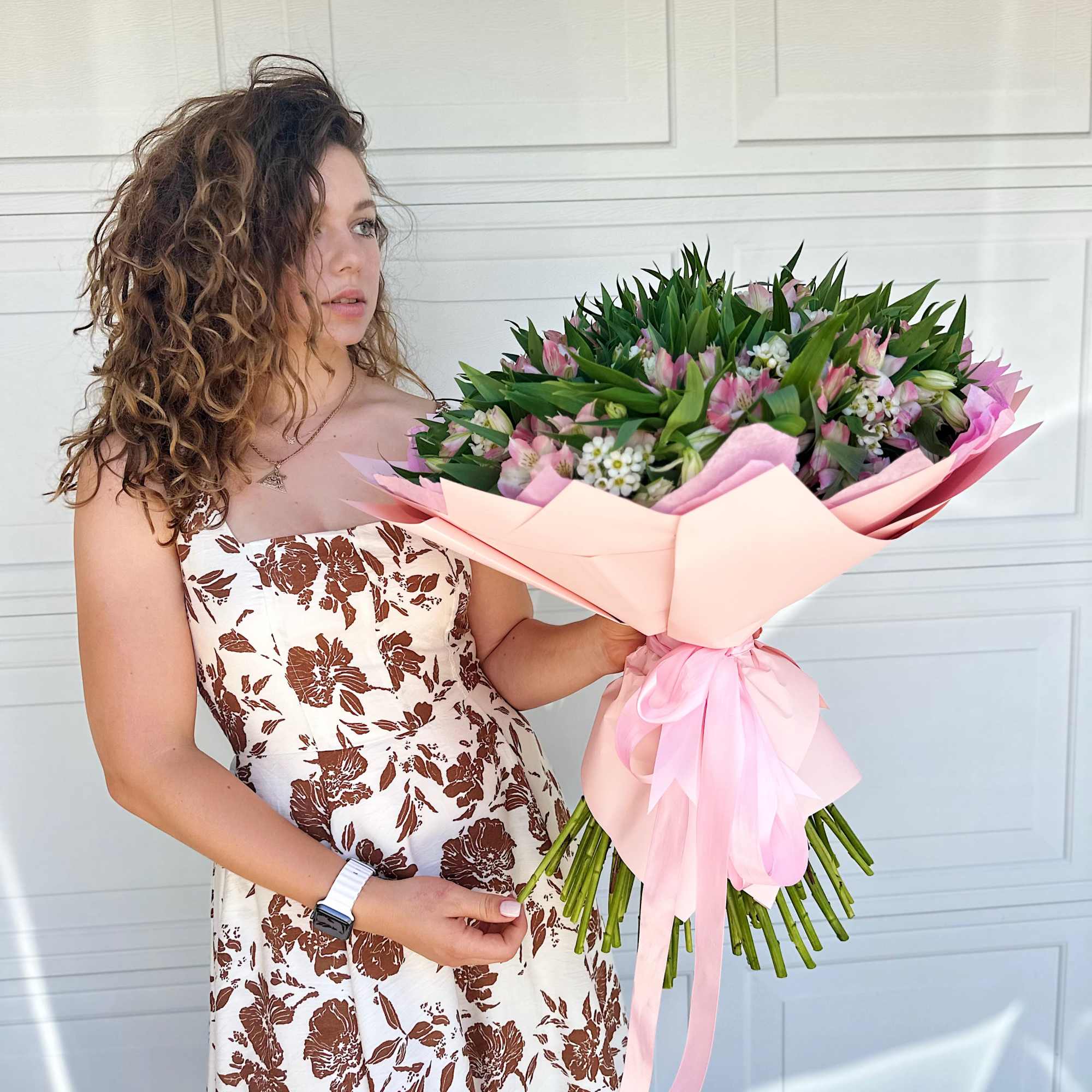 Woman holding a large pink bouquet with green foliage
