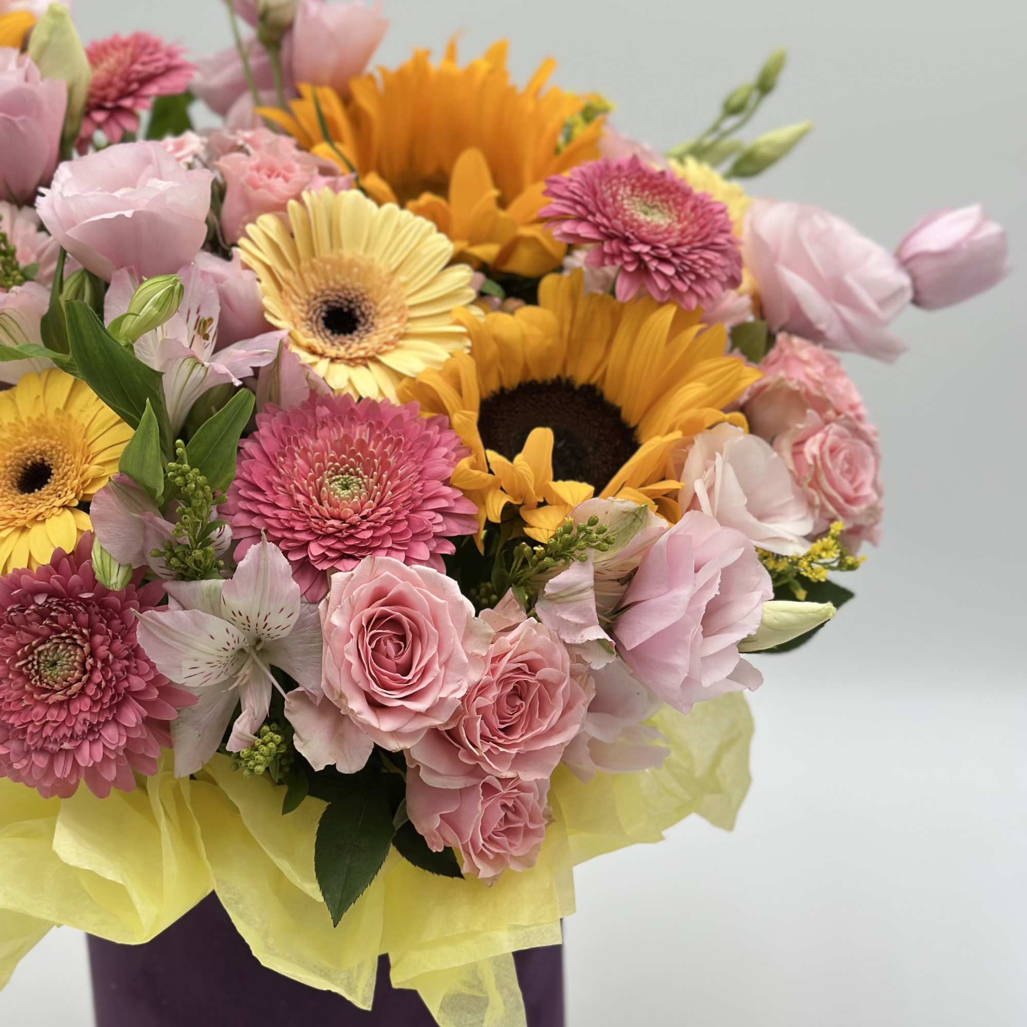 Mixed bouquet with sunflowers, pink roses, and gerbera daisies in a purple wrap