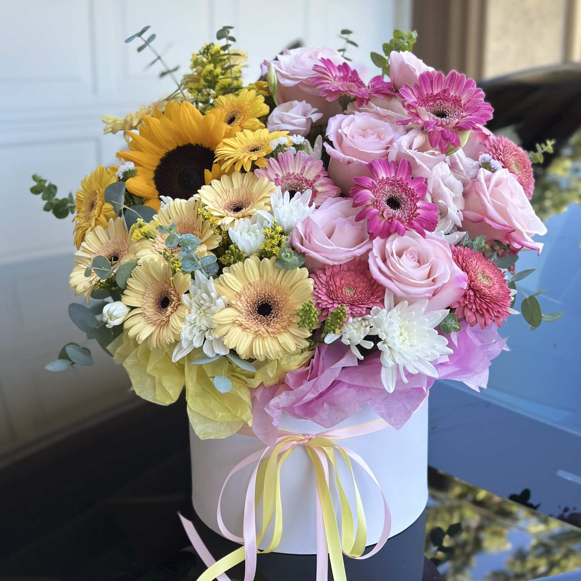 Bouquet of pink roses, gerbera daisies, and sunflowers in a white hat box