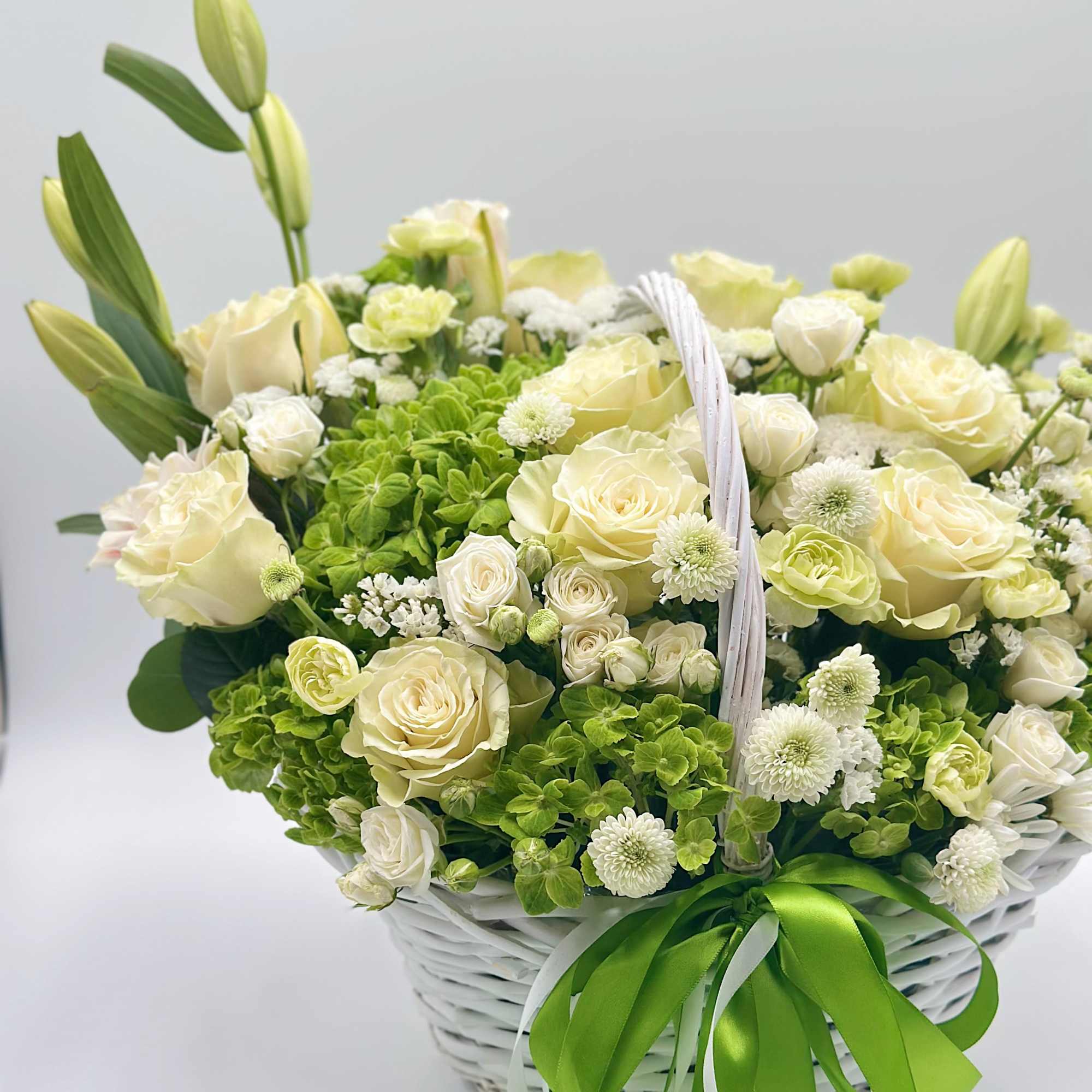 White and pale yellow flowers arranged in a white basket with green ribbon