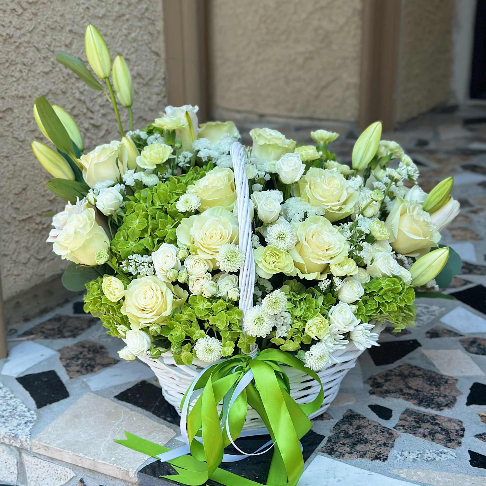 White basket of pale yellow roses and lilies with green ribbon