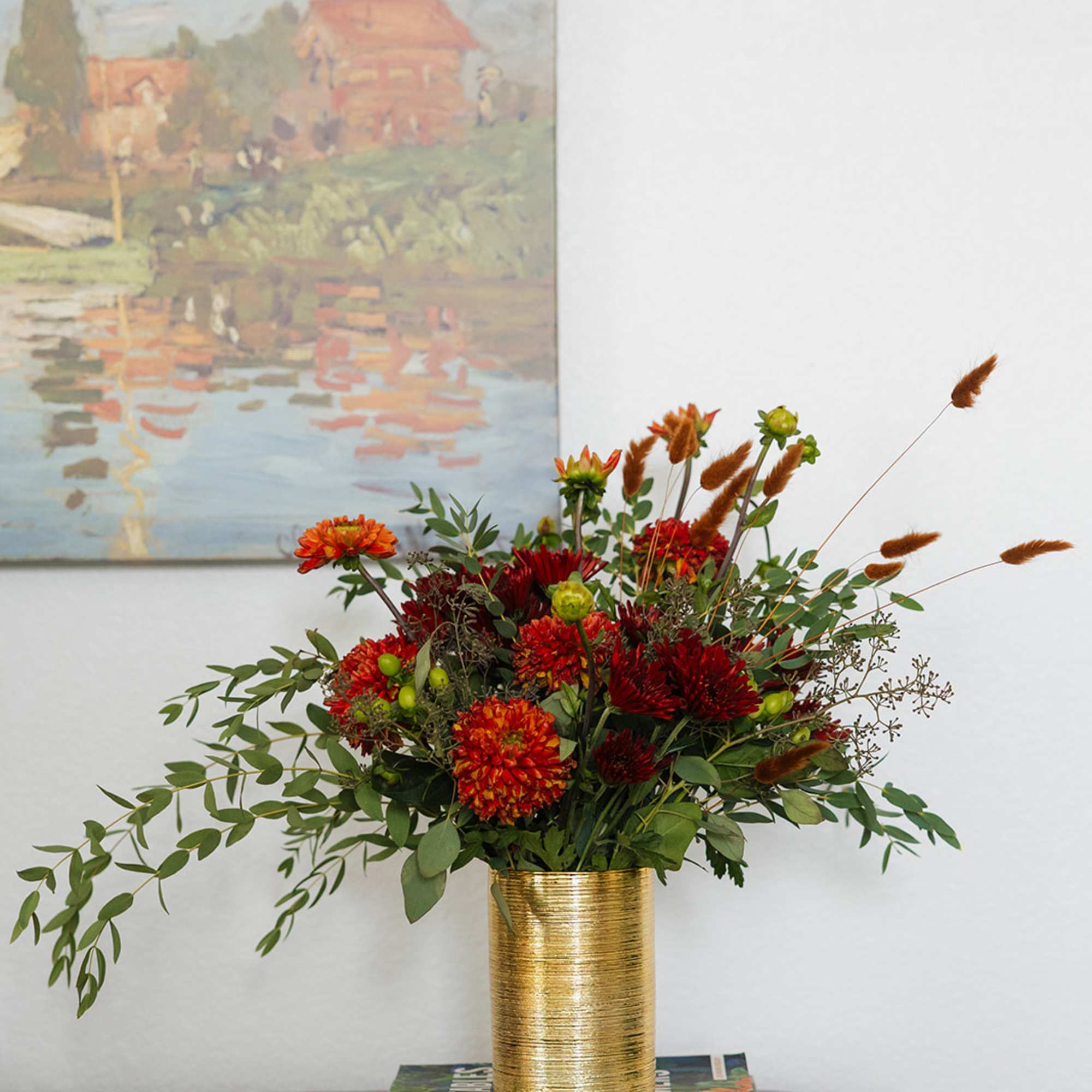Red and orange floral arrangement in a gold vase on stacked books