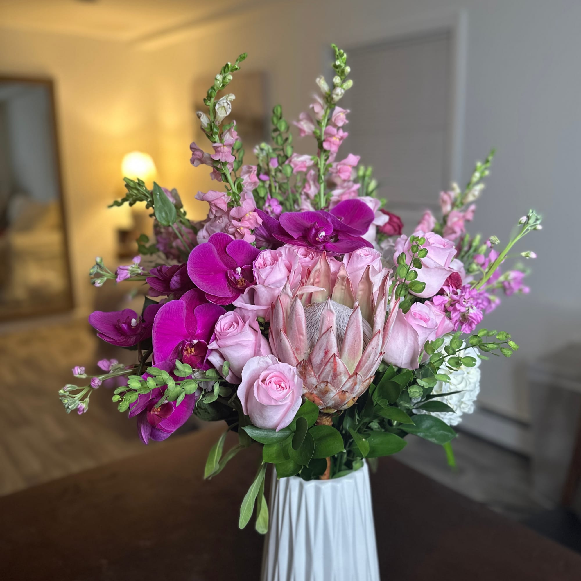 Pink and purple floral arrangement in a white vase with a protea centerpiece