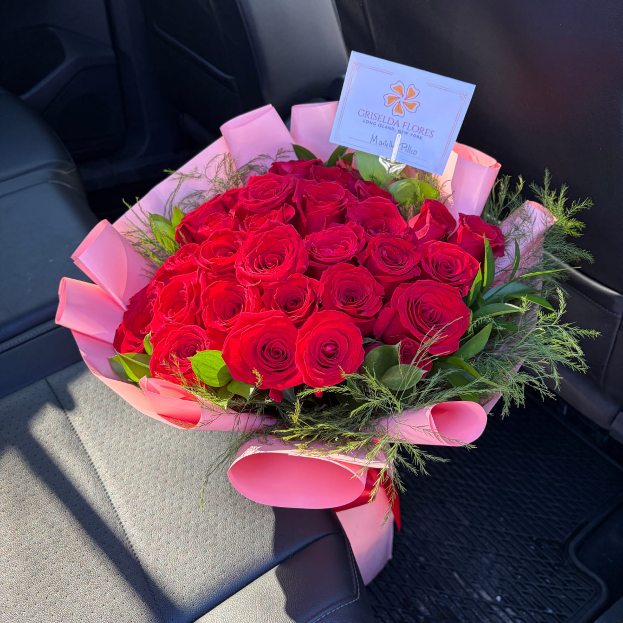 Bouquet of red roses wrapped in pink paper with greenery