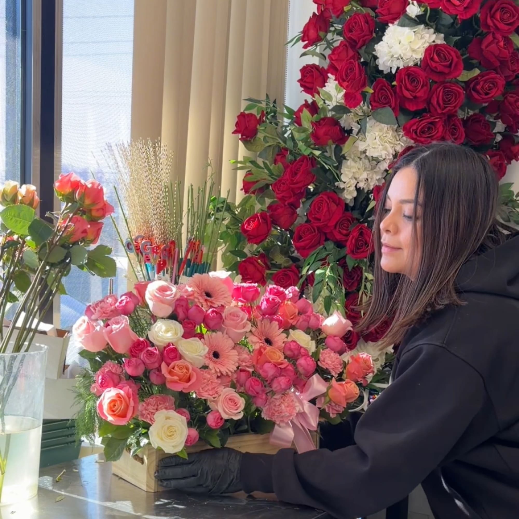 Woman arranging pink and red roses in a wooden box with a ribbon.