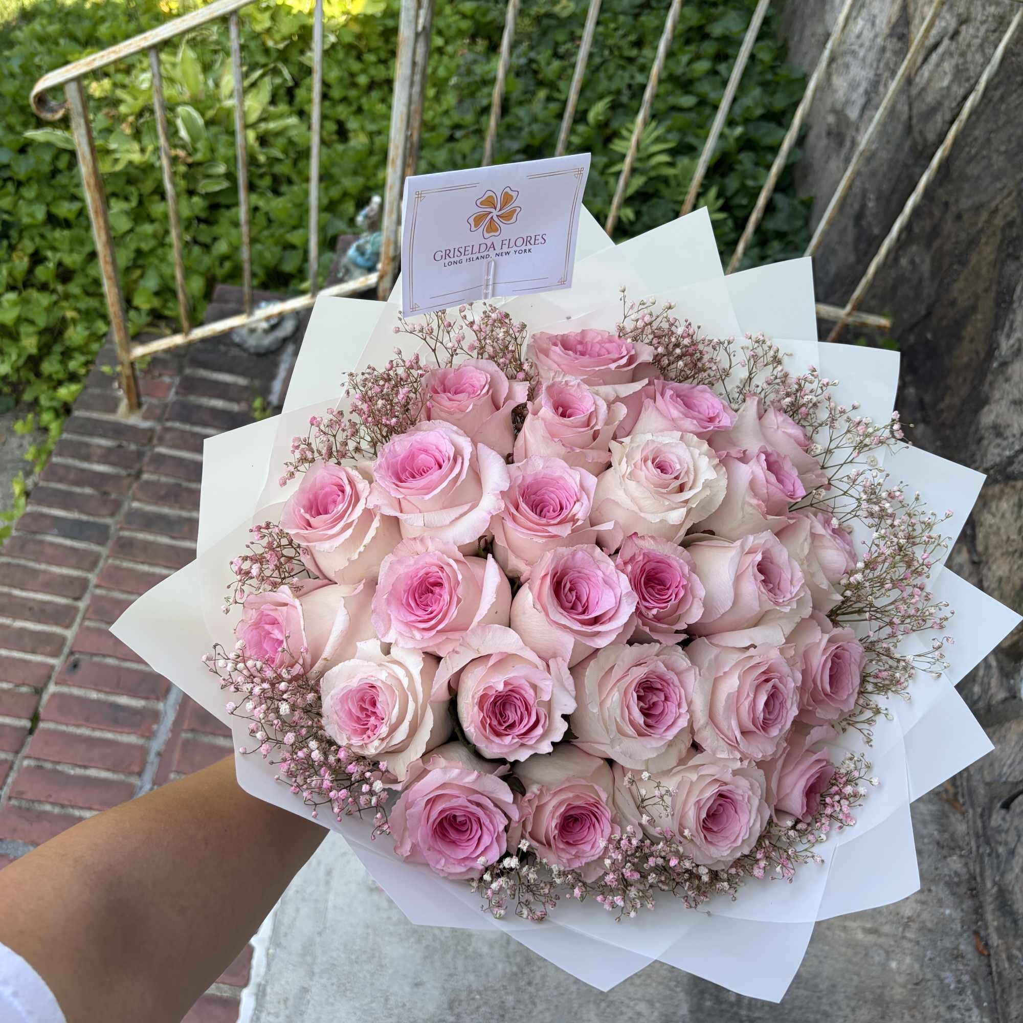 Handheld bouquet of pink roses wrapped in white paper