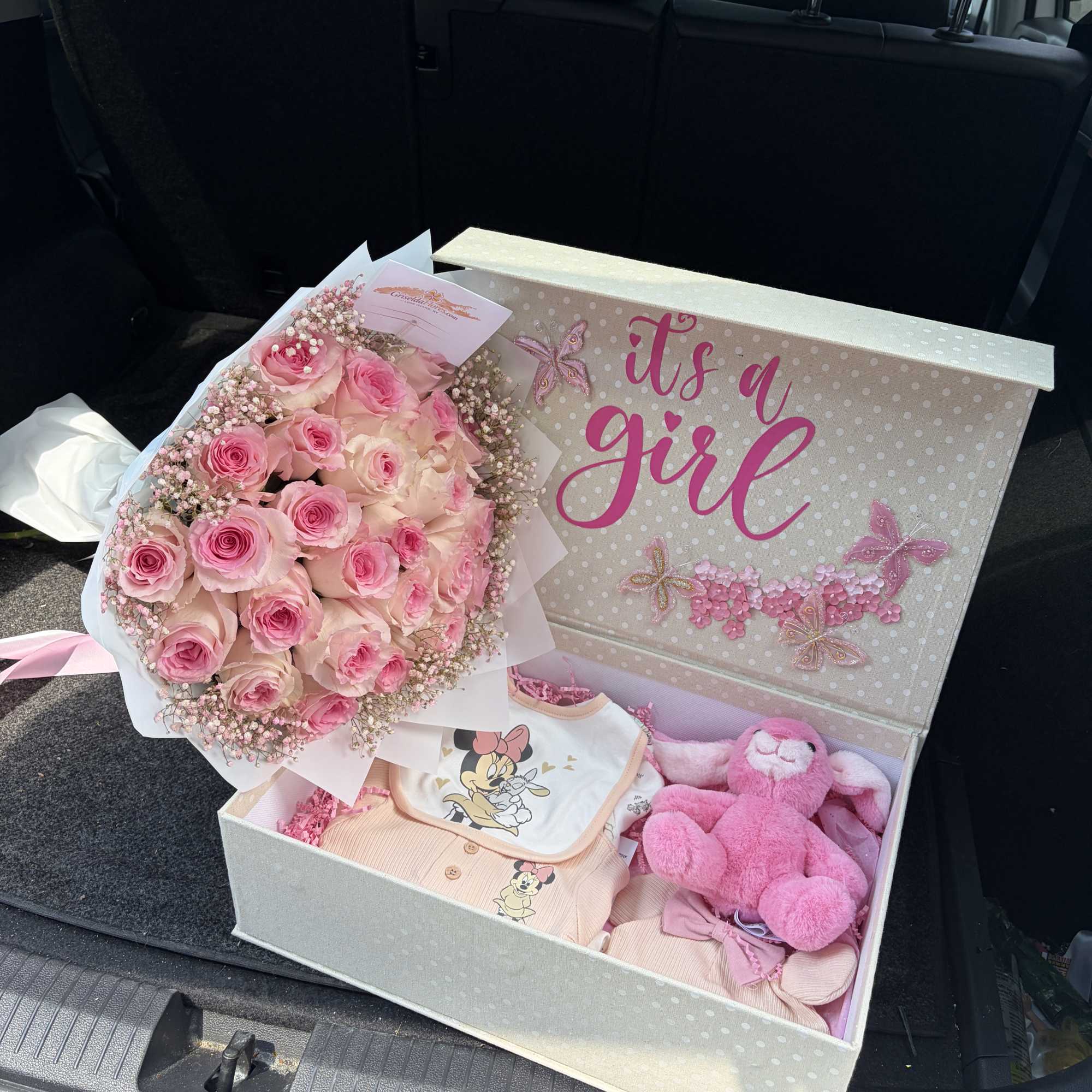 Pink rose bouquet beside a gift box with baby clothes and a plush toy