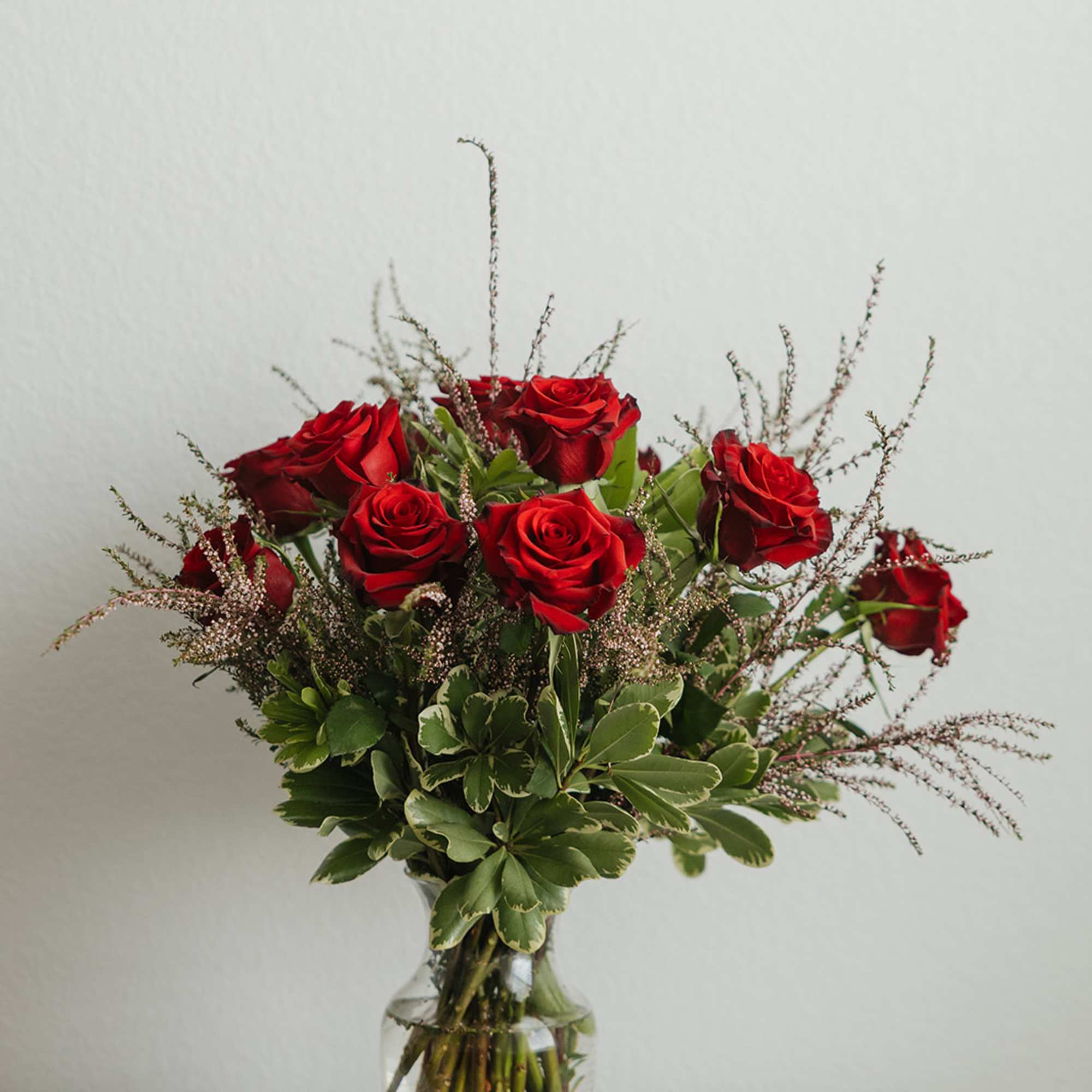 Red roses arranged in a clear glass vase with greenery