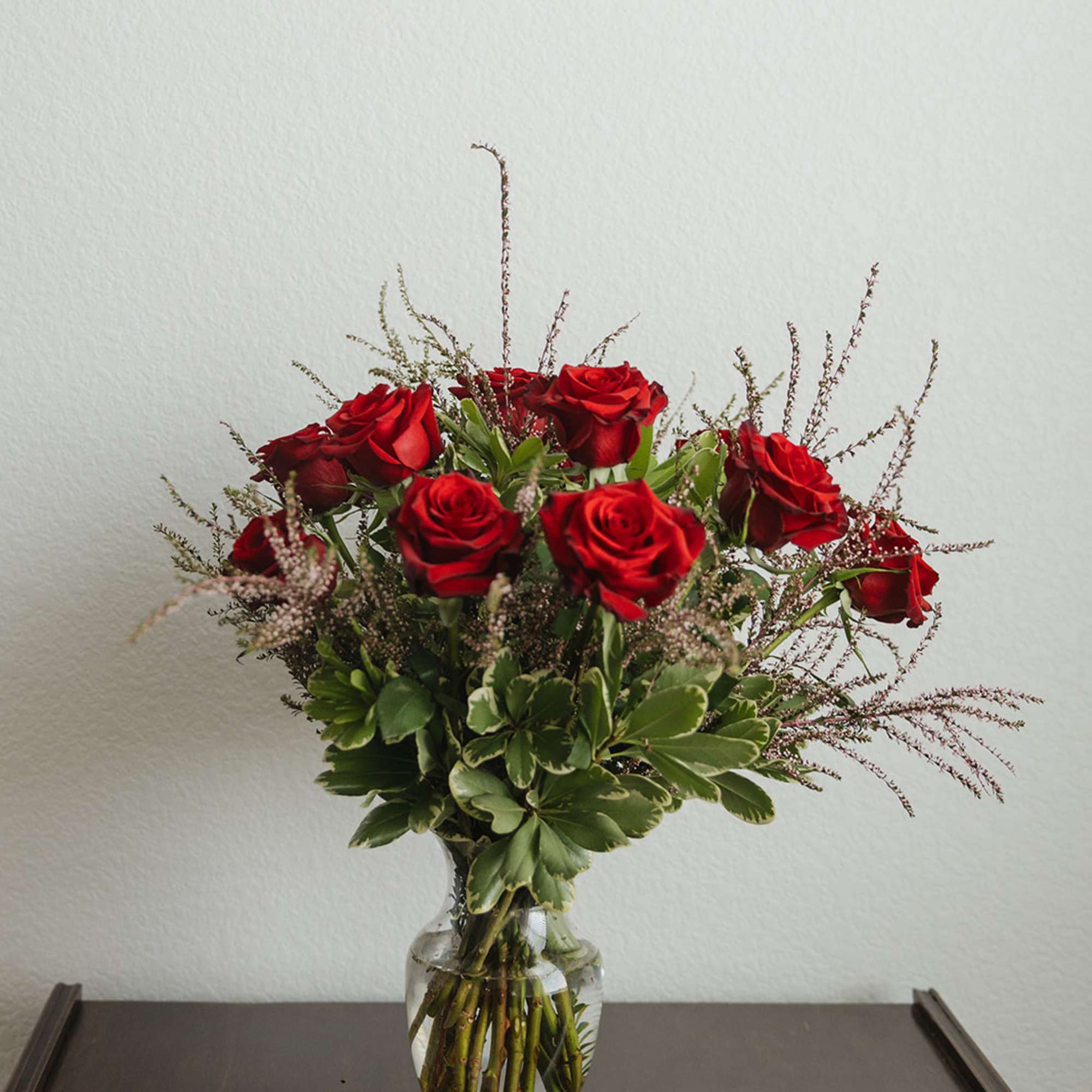 Red roses arranged in a clear glass vase with greenery, photo 2 of 3
