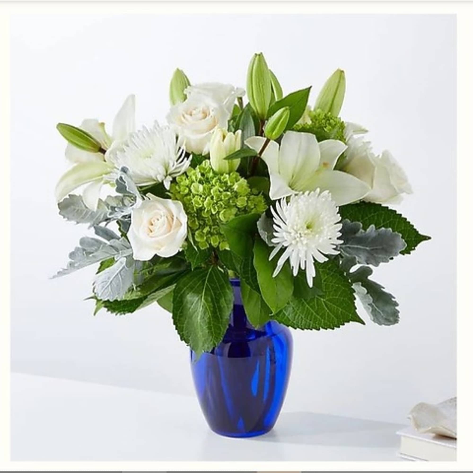 White lilies and roses arranged in a blue glass vase