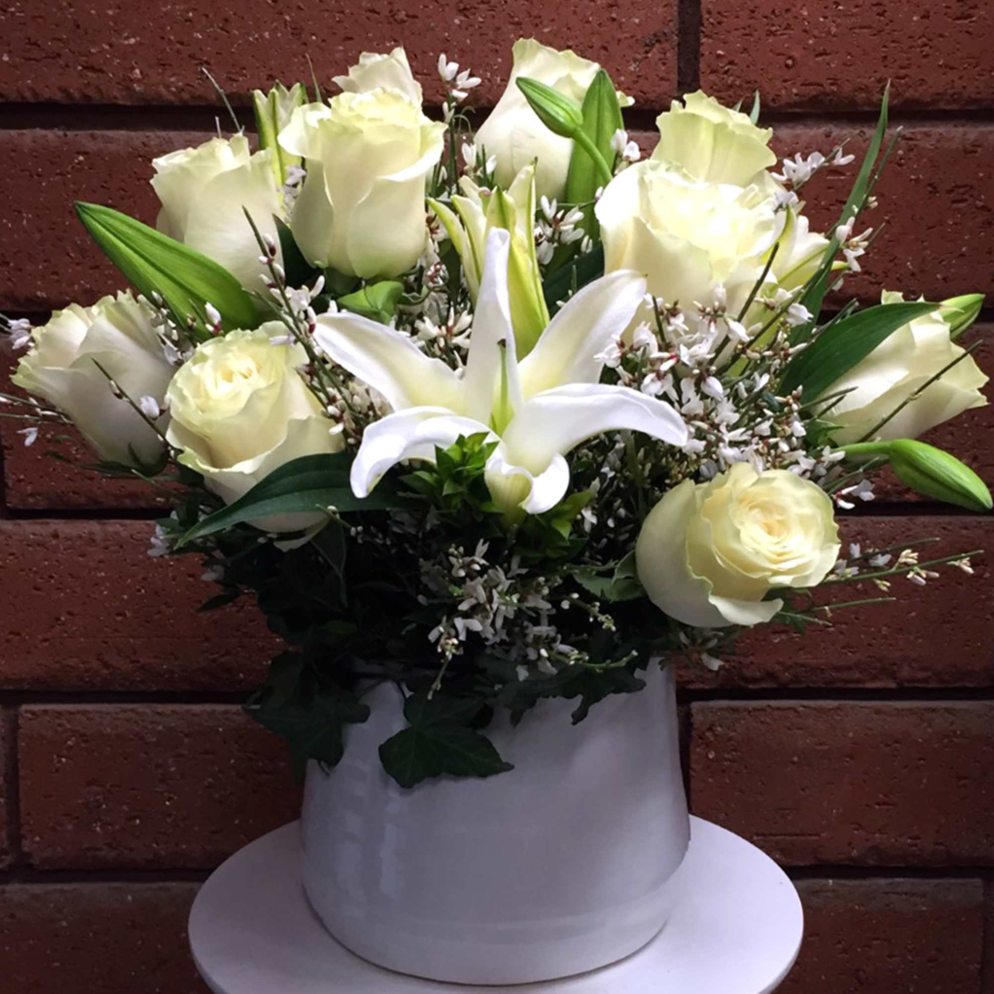 White roses and a white lily in a white hatbox-style container