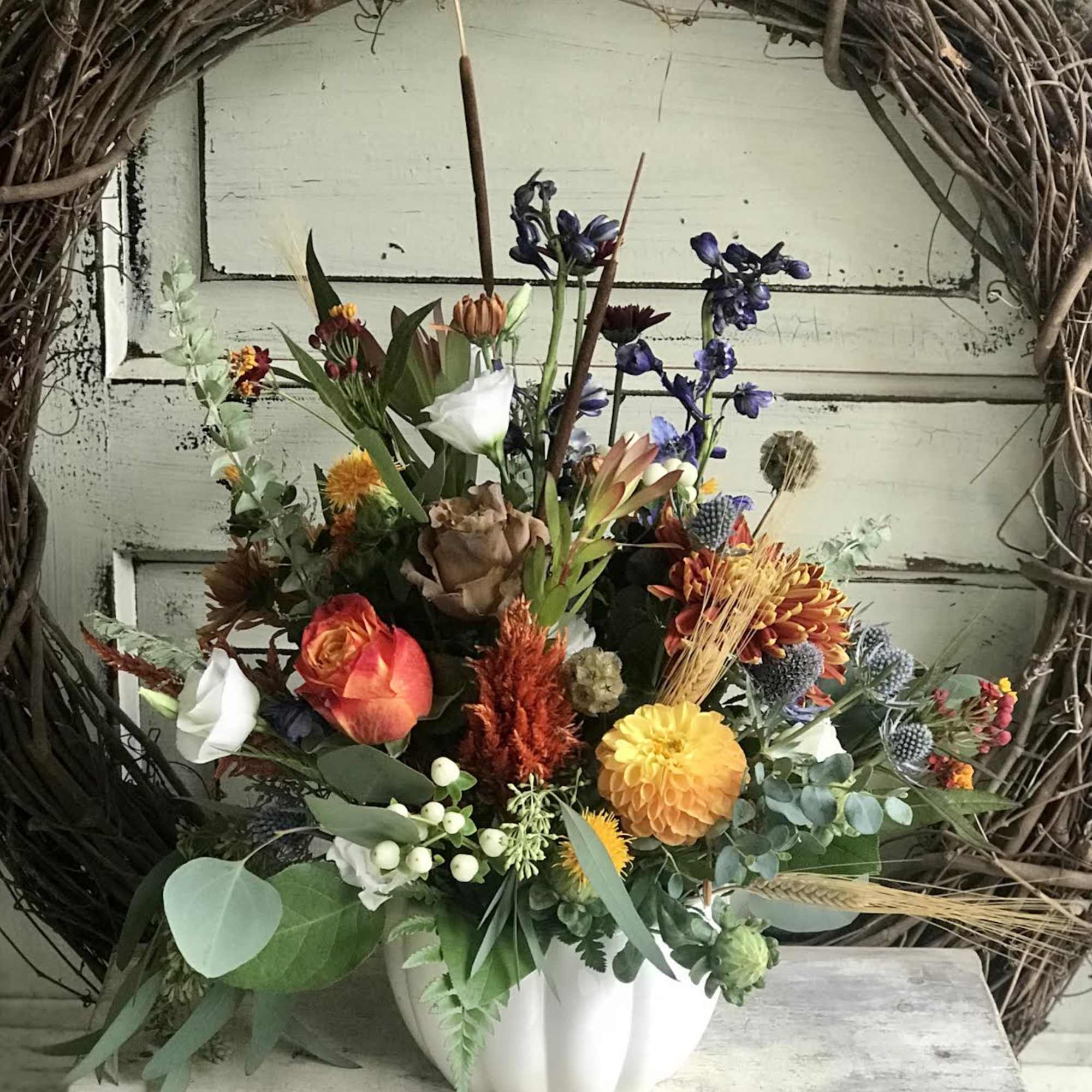 Mixed floral arrangement in a white pumpkin-shaped vase with orange, yellow, and purple blooms