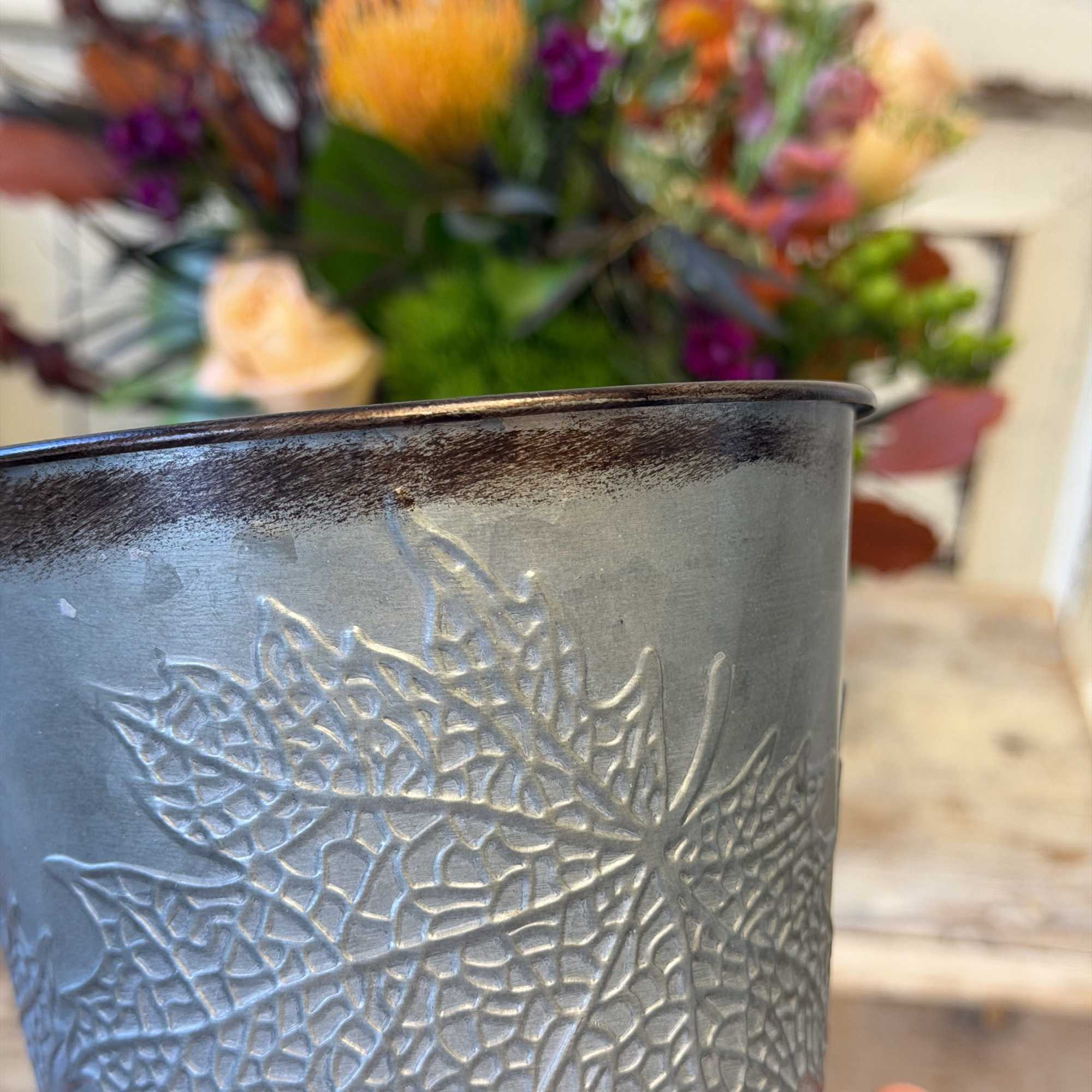 Embossed metal vase held in front of a colorful flower arrangement