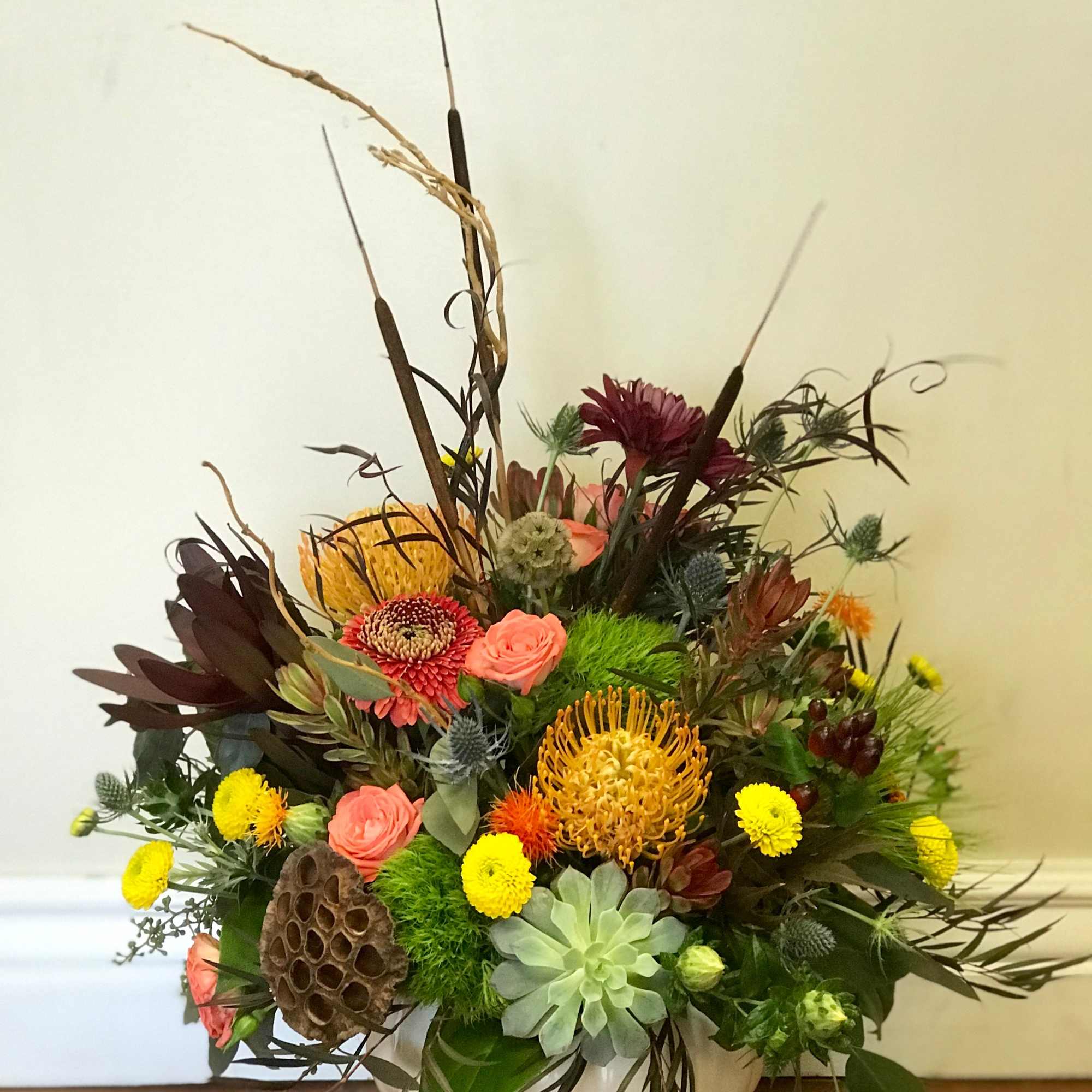 Mixed floral arrangement in a white bowl vase with tall dried accents