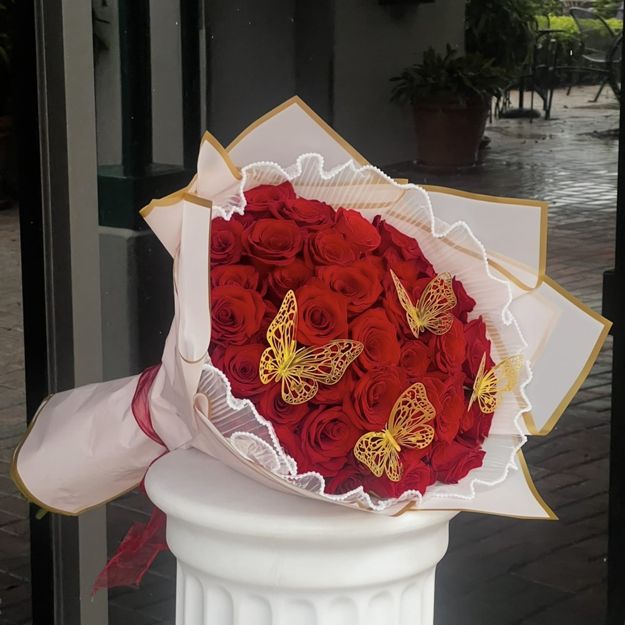 Bouquet of red roses wrapped in white paper with gold trim and butterfly accents