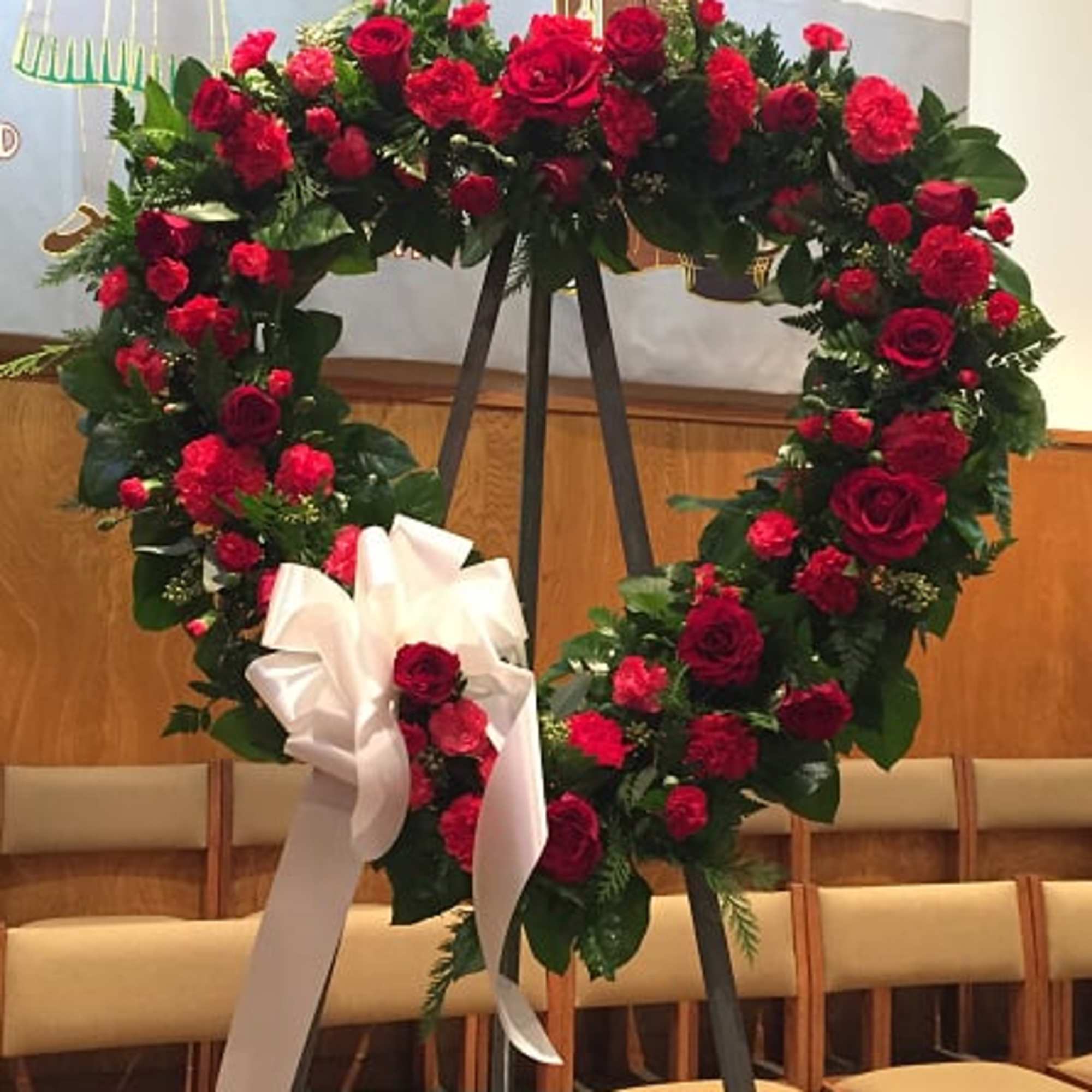 Heart-shaped red rose wreath on an easel with a white ribbon bow