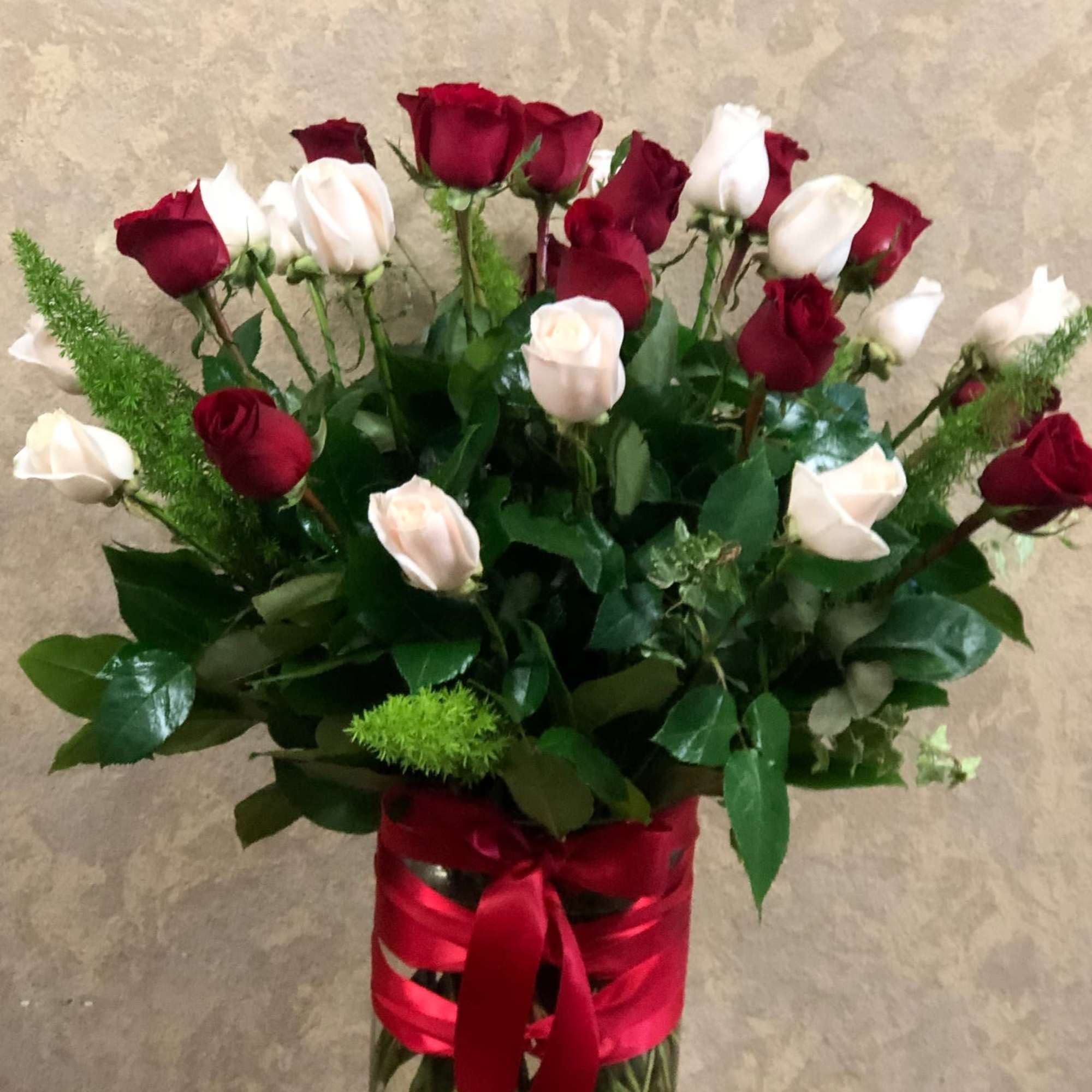 Tall vase of red and white roses with greenery and red ribbon around the clear glass vase