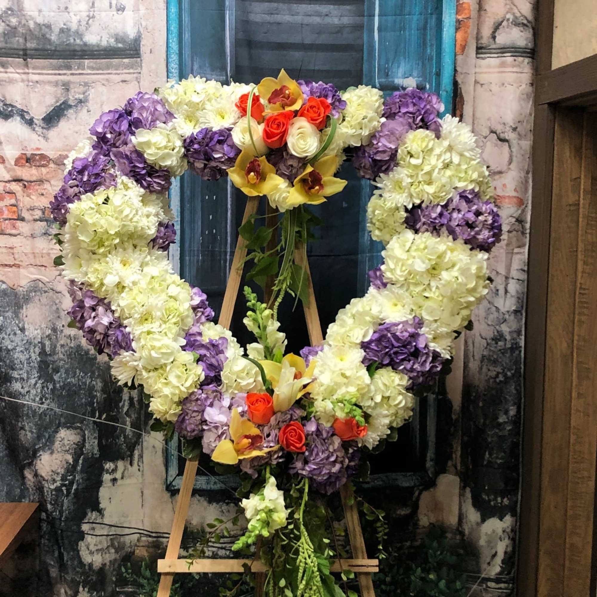 Heart-shaped floral wreath on an easel with purple, white, and yellow flowers