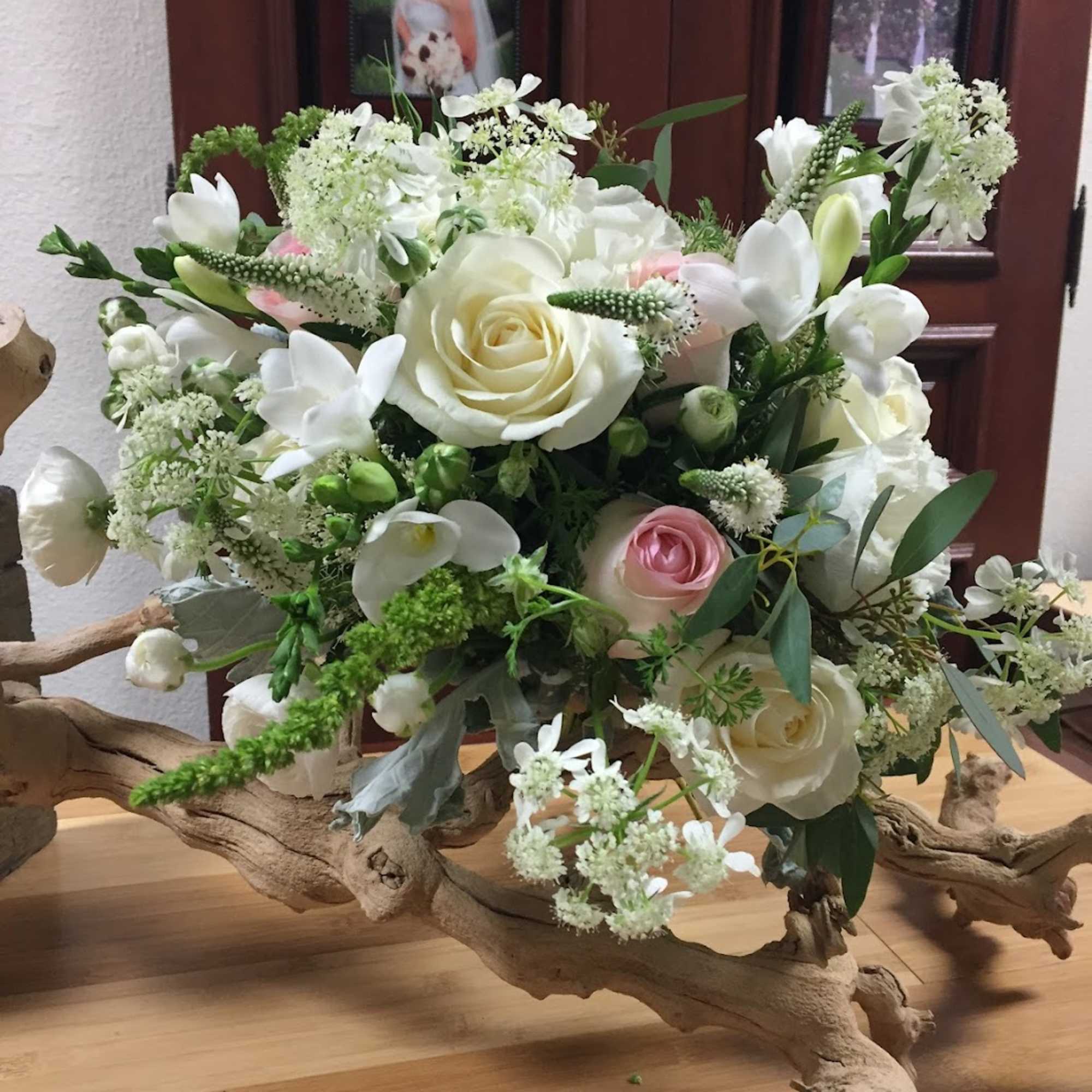 White and blush roses arranged with small white blooms on driftwood.