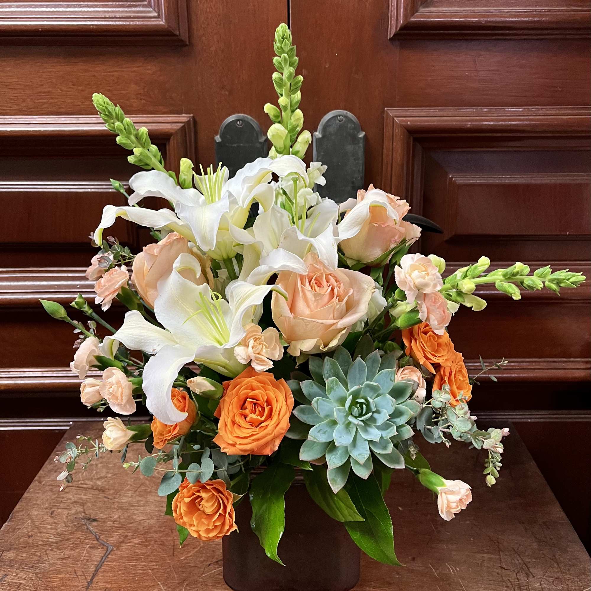 Arrangement of white lilies, peach roses, and orange roses in a dark vase