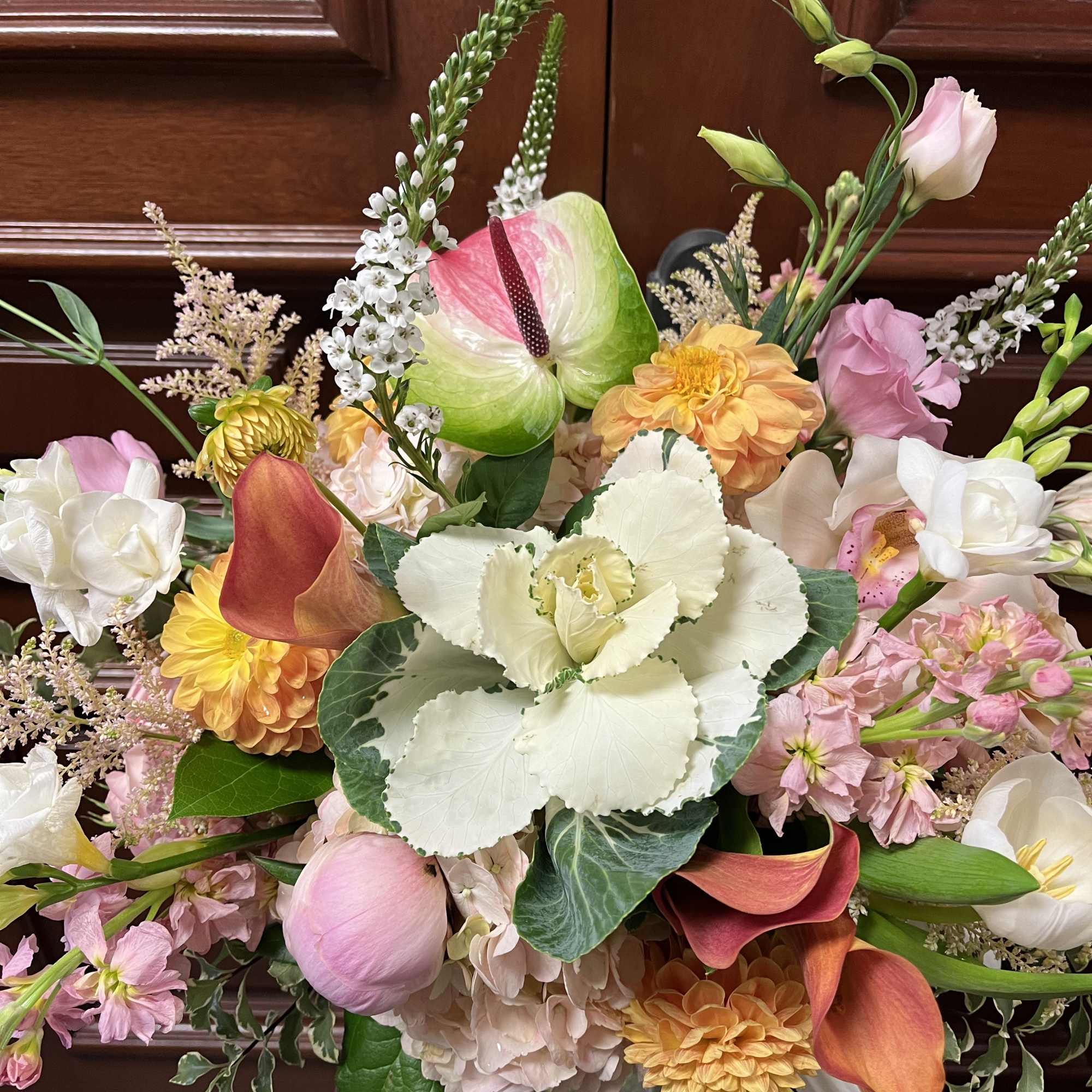 Lush mixed bouquet of pink, peach, and white flowers with calla lilies in a clear glass vase
