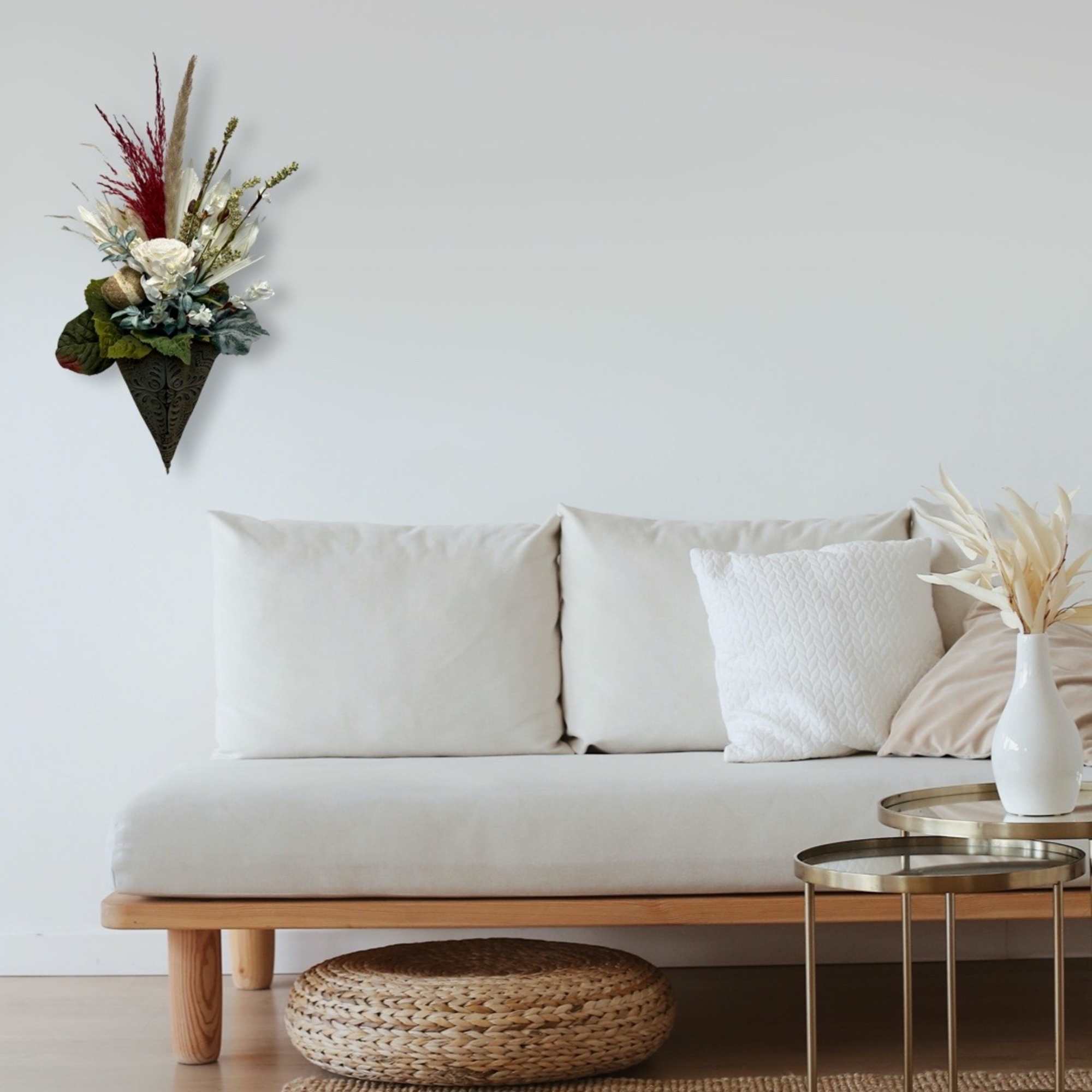 Wall-mounted dried floral arrangement above a cream sofa with a vase of dried stems nearby