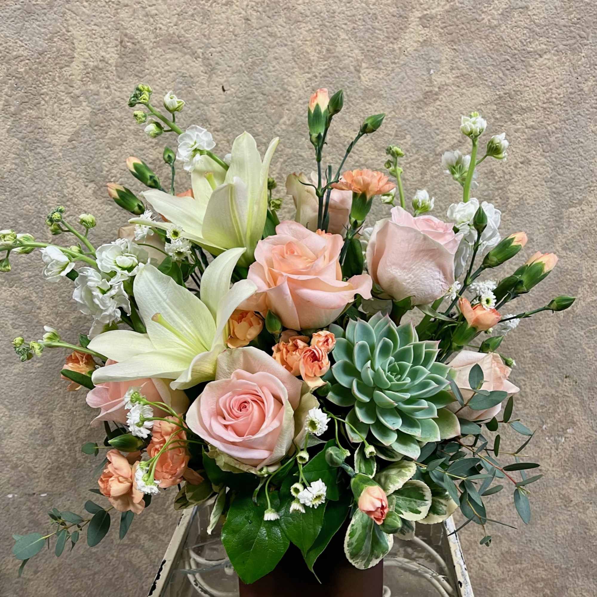 Pastel bouquet with roses, lilies, and a succulent in a square vase