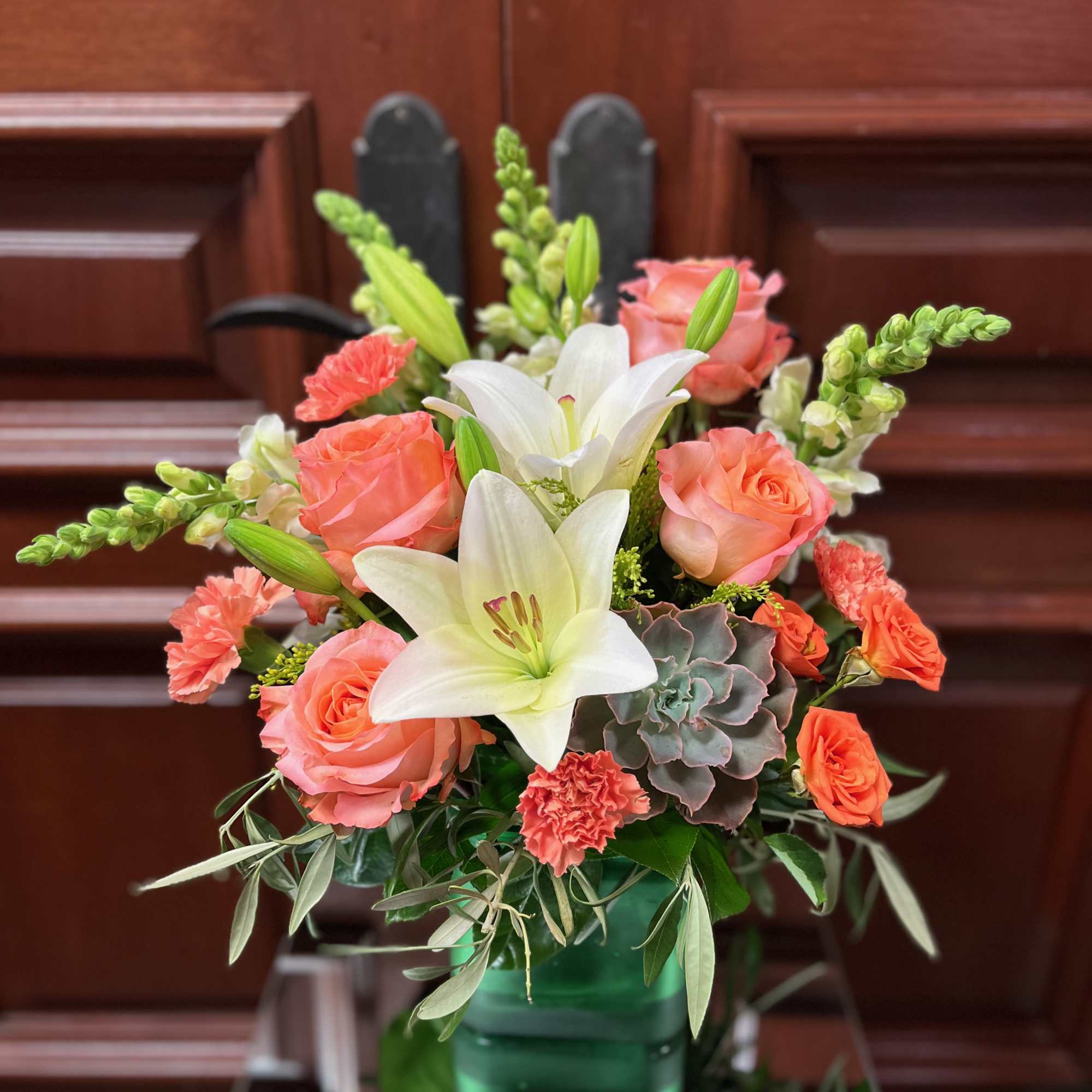 Coral roses and white lilies arranged in a green vase