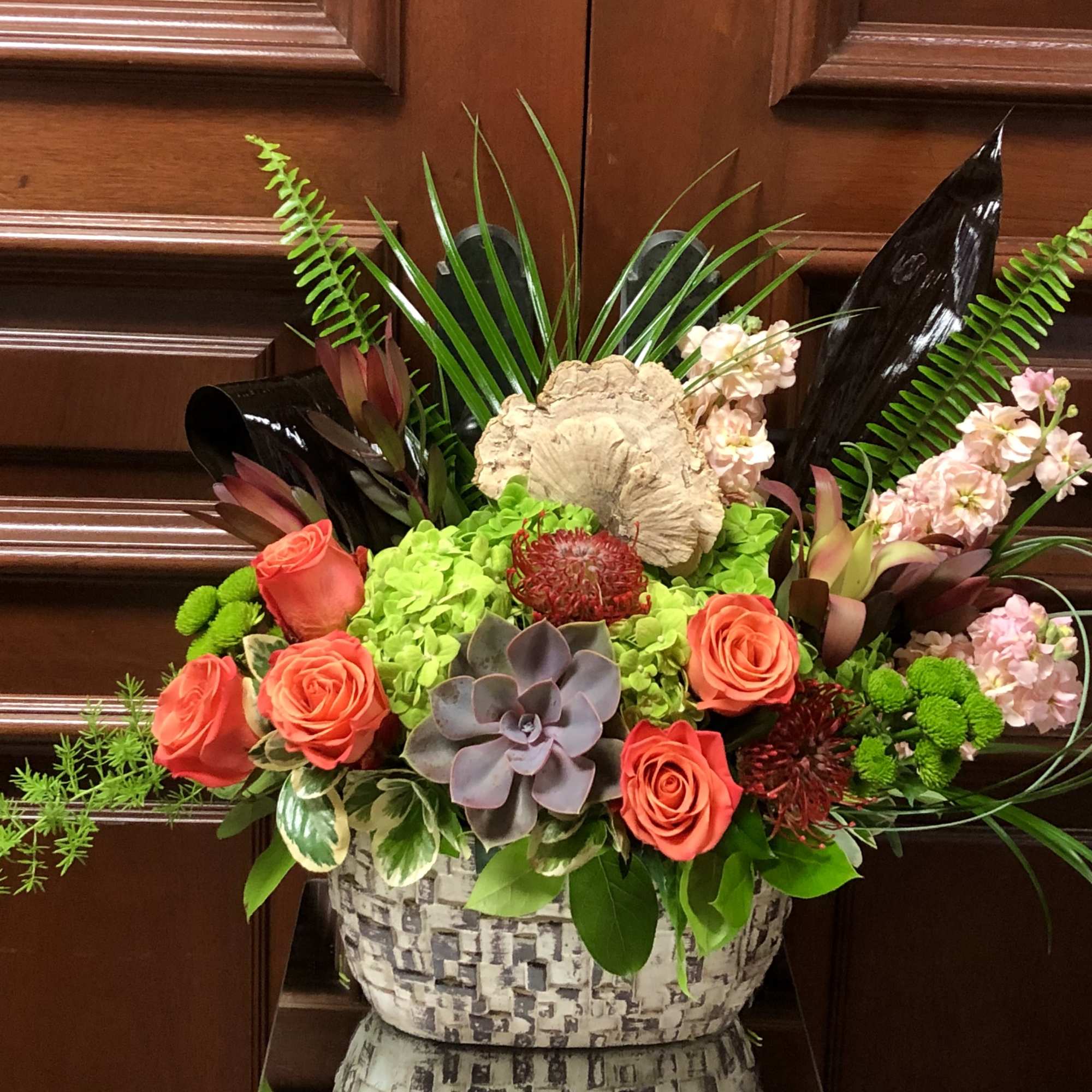 Mixed floral arrangement in a patterned basket with coral roses and succulents