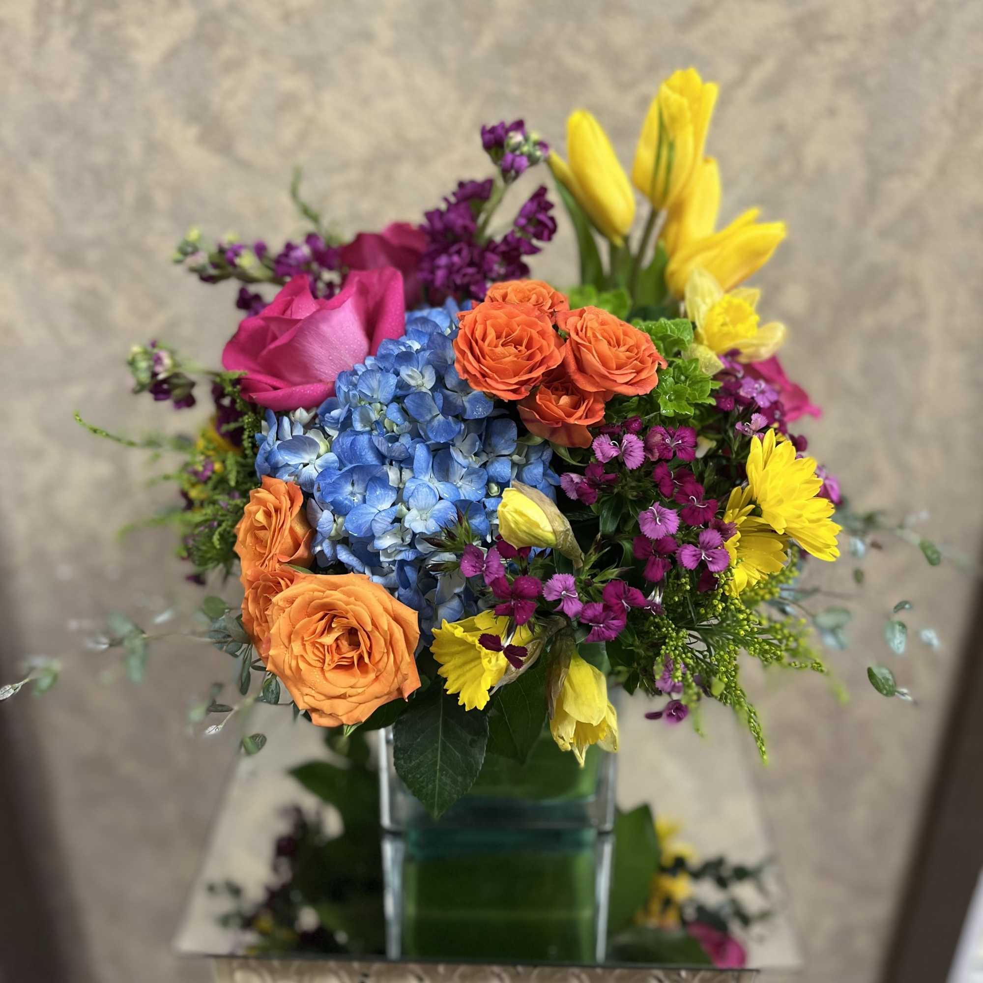 Colorful bouquet with roses, hydrangea, and yellow blooms in a glass vase