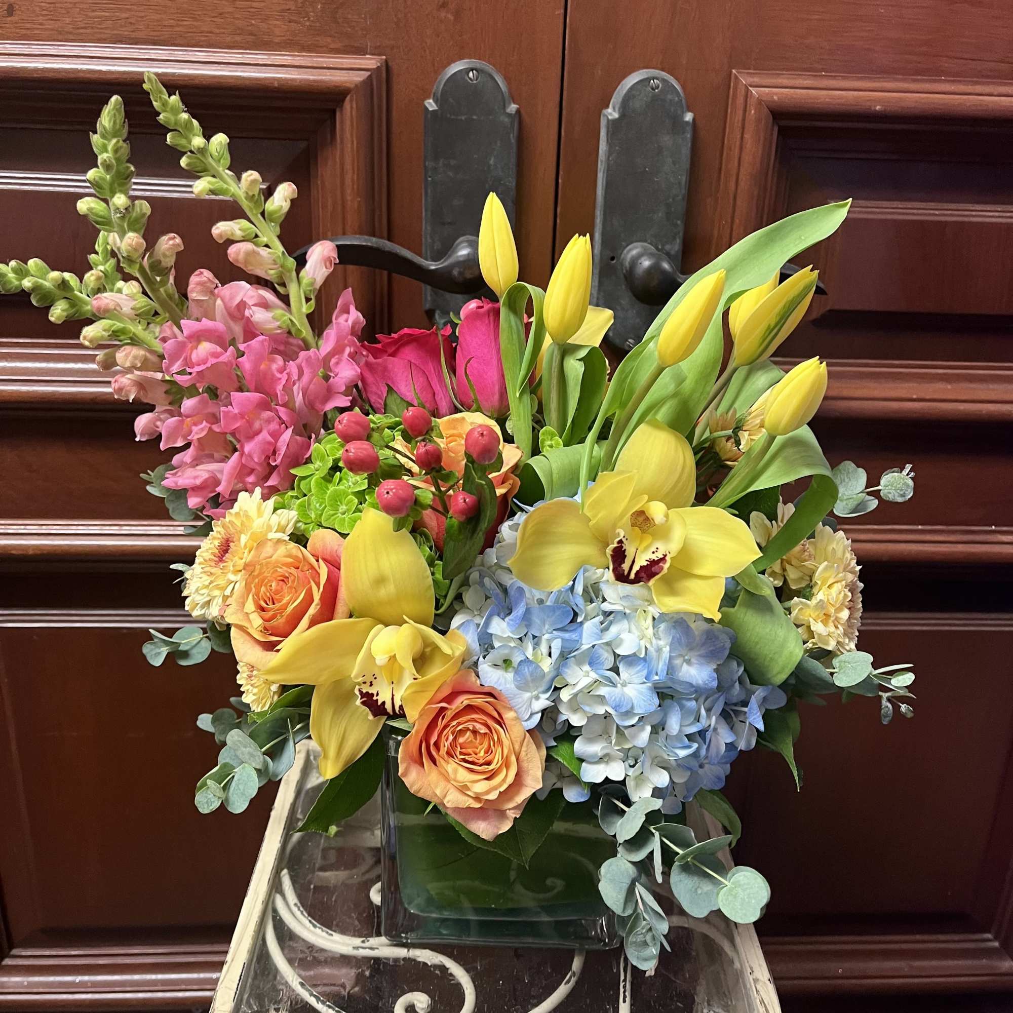 Mixed bouquet in a glass vase with yellow orchids, pink snapdragons, and blue hydrangeas