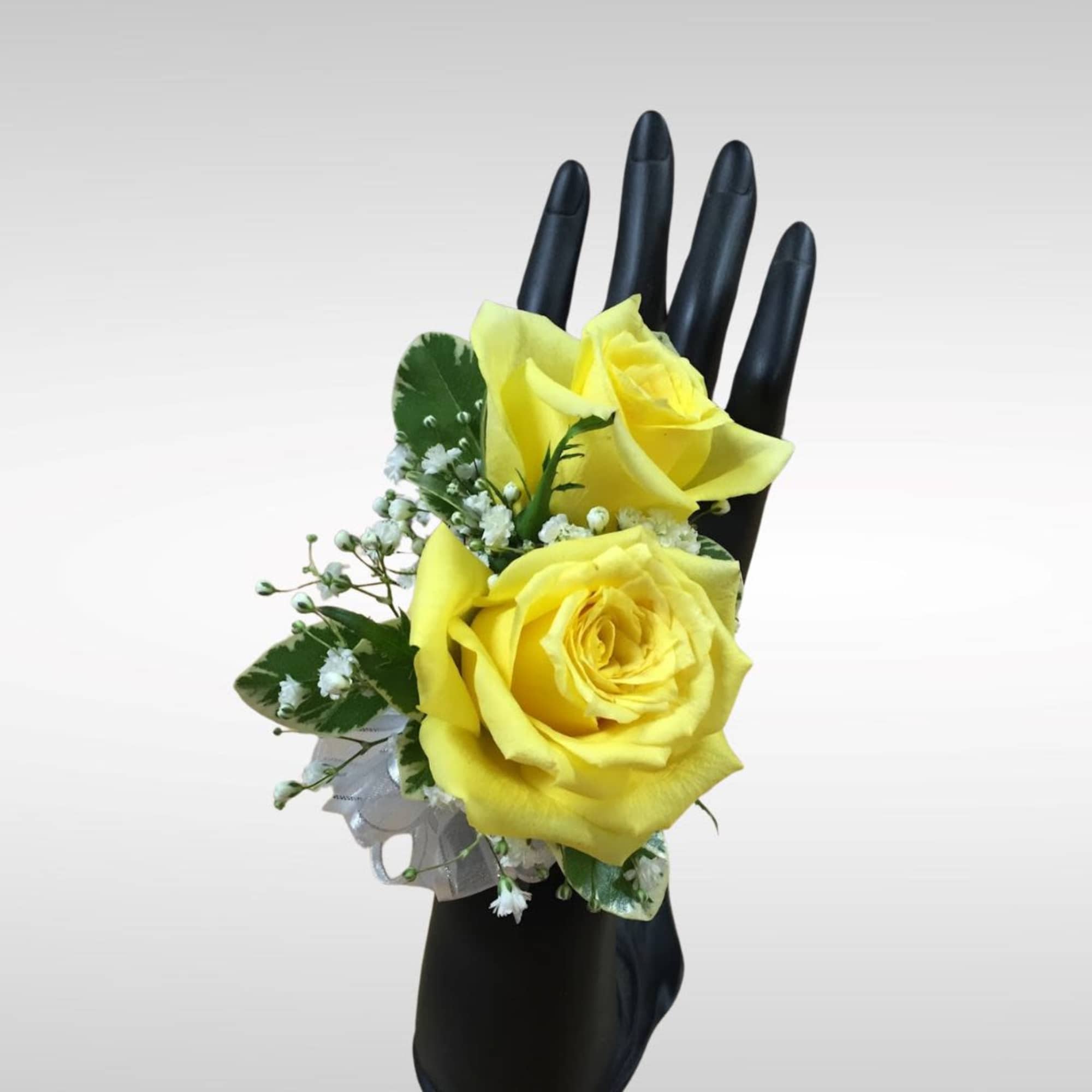 Yellow rose wrist corsage with white accents on a black display hand