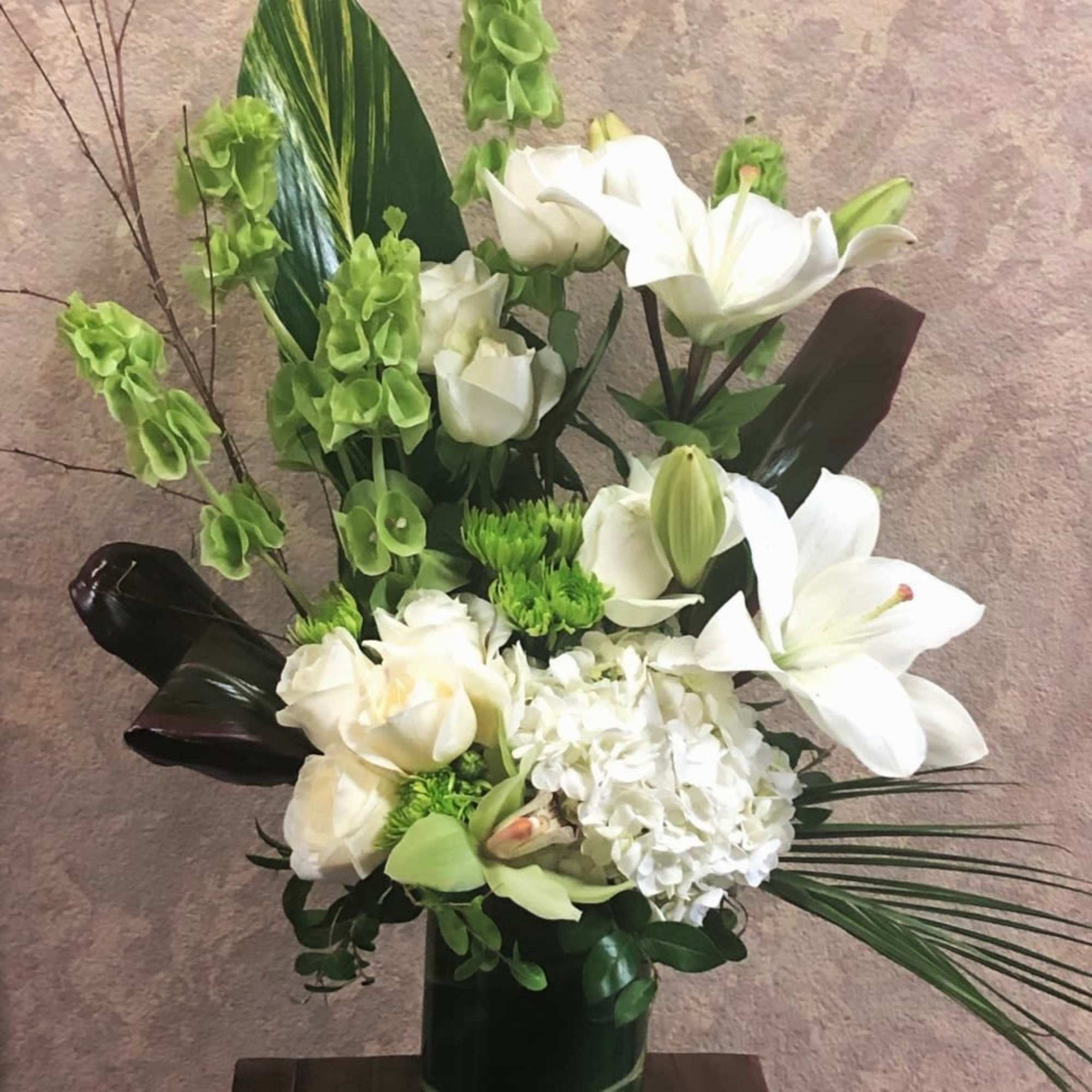 White lilies and roses arranged in a tall dark vase with green accents