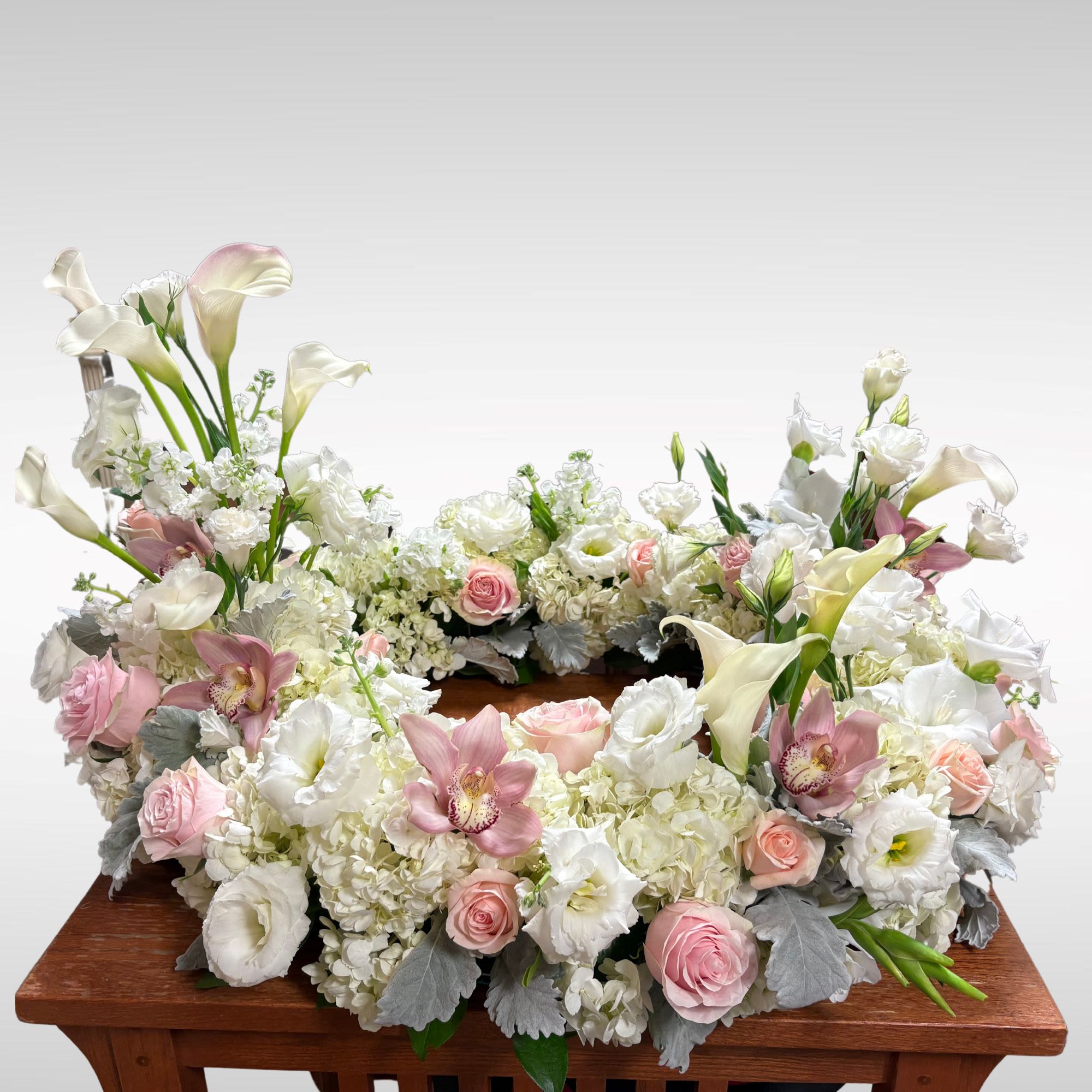 Floral wreath with white calla lilies, pink roses, and white orchids on a wooden stand