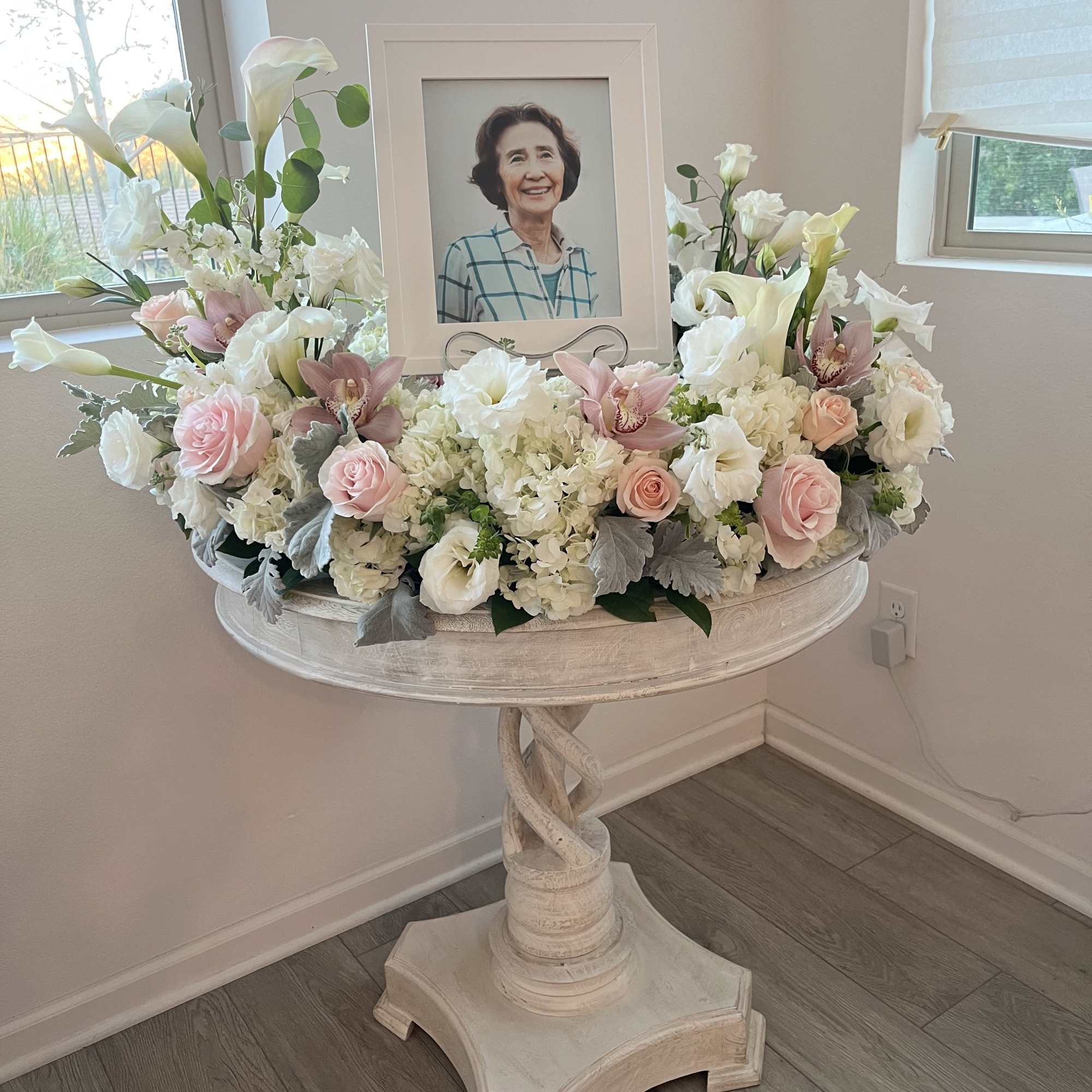 Sympathy floral arrangement around a framed portrait on a pedestal table