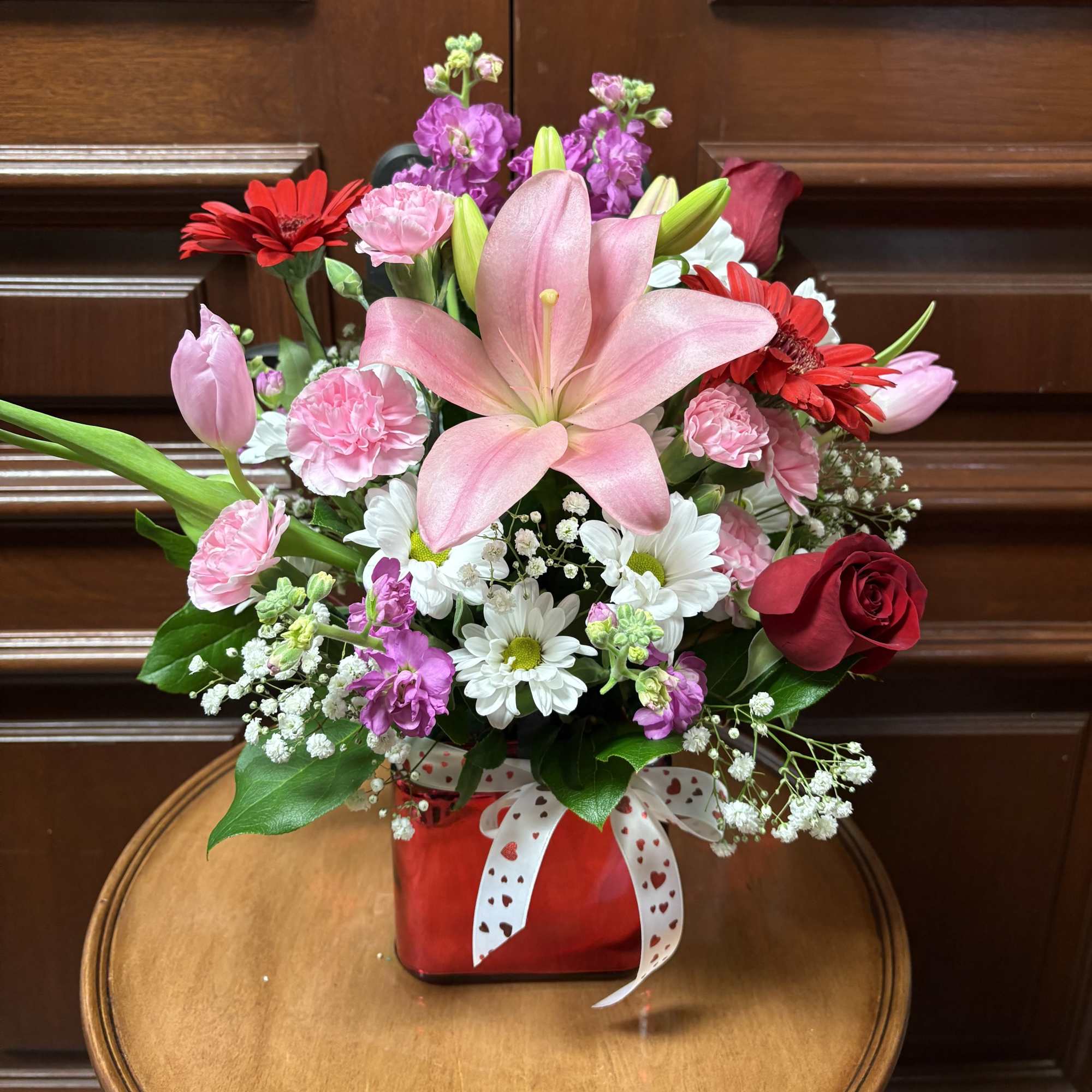Mixed bouquet with pink lilies, red roses, and white daisies in a red vase