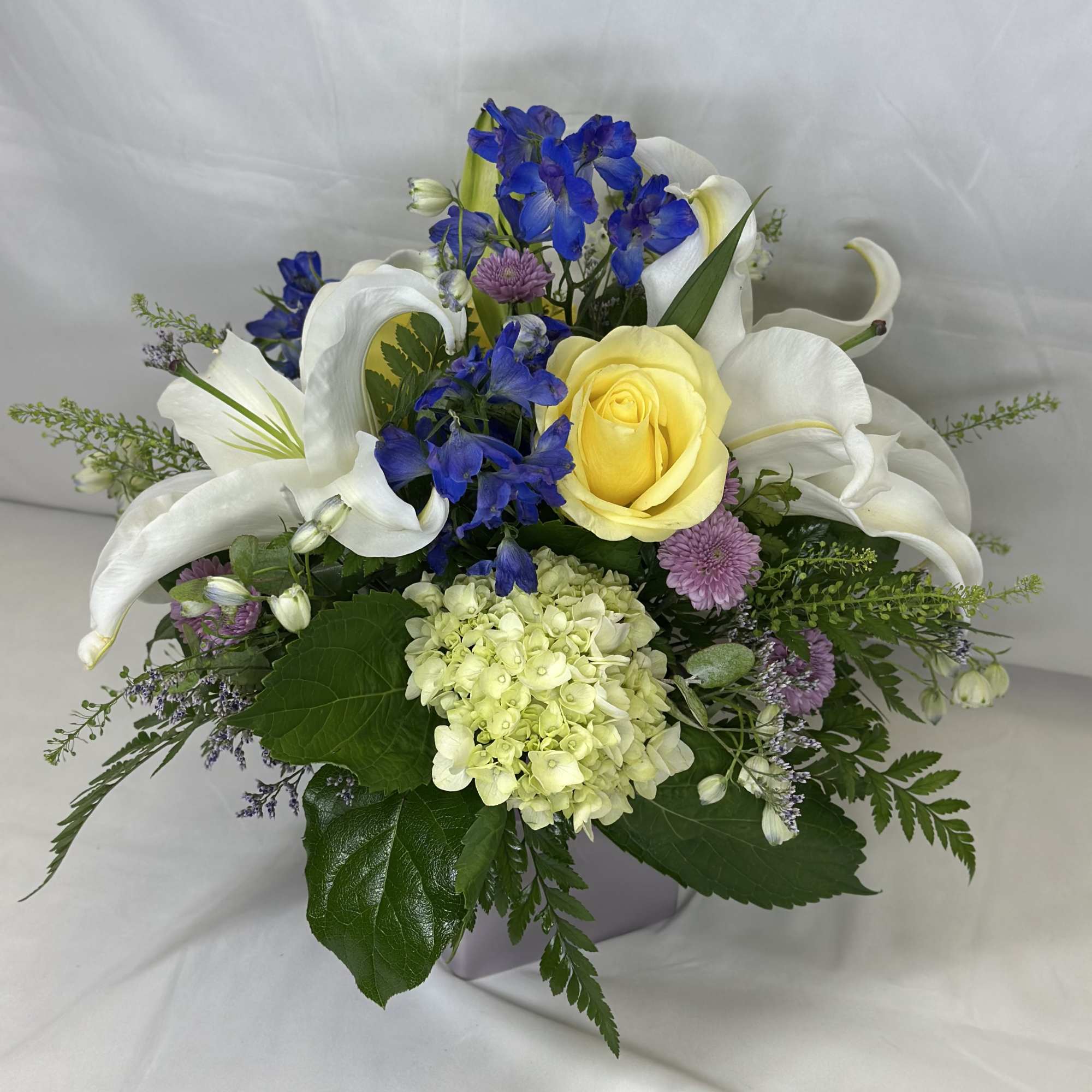 Bouquet of white lilies, a yellow rose, and blue flowers in a vase