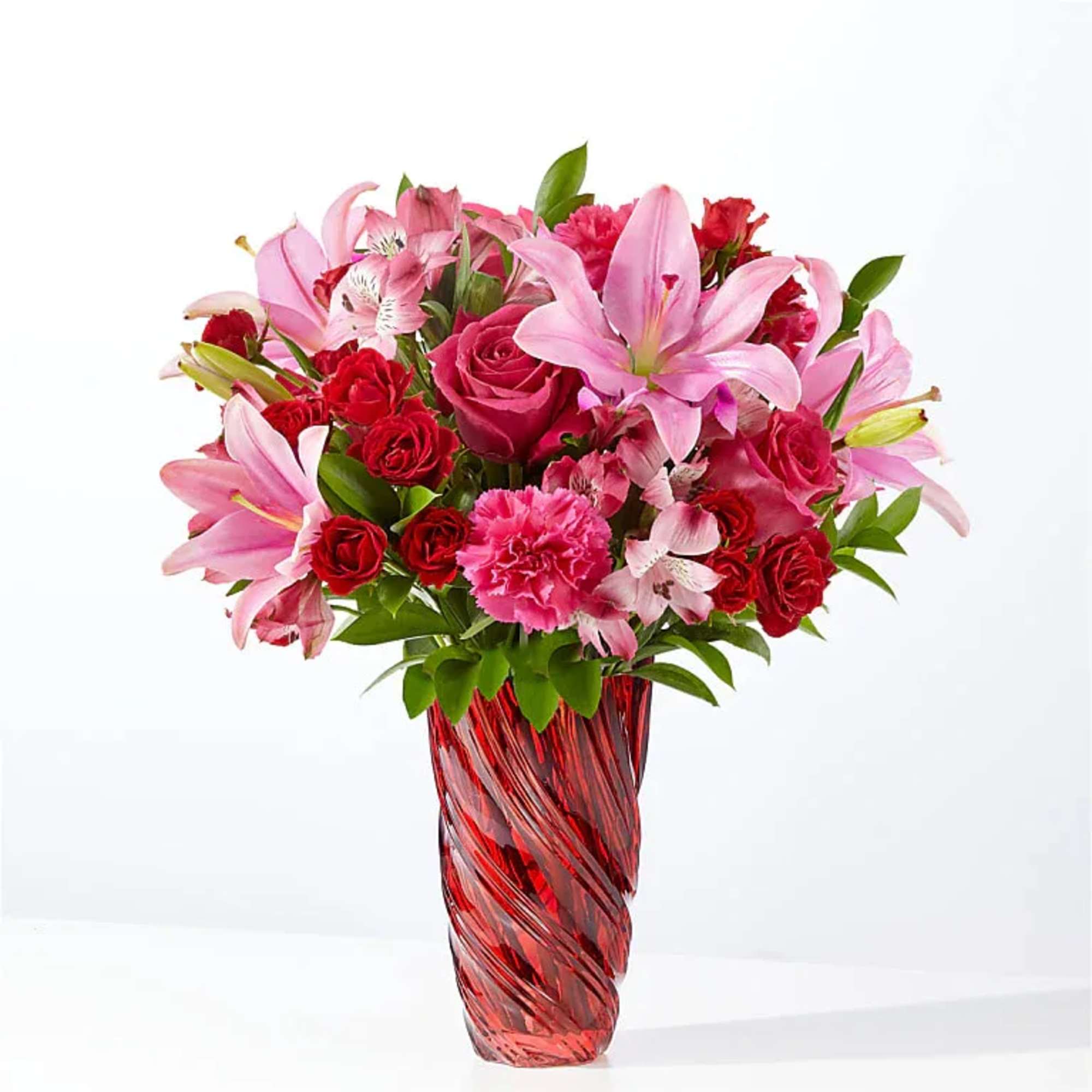 Pink lilies and red roses arranged in a red glass vase.