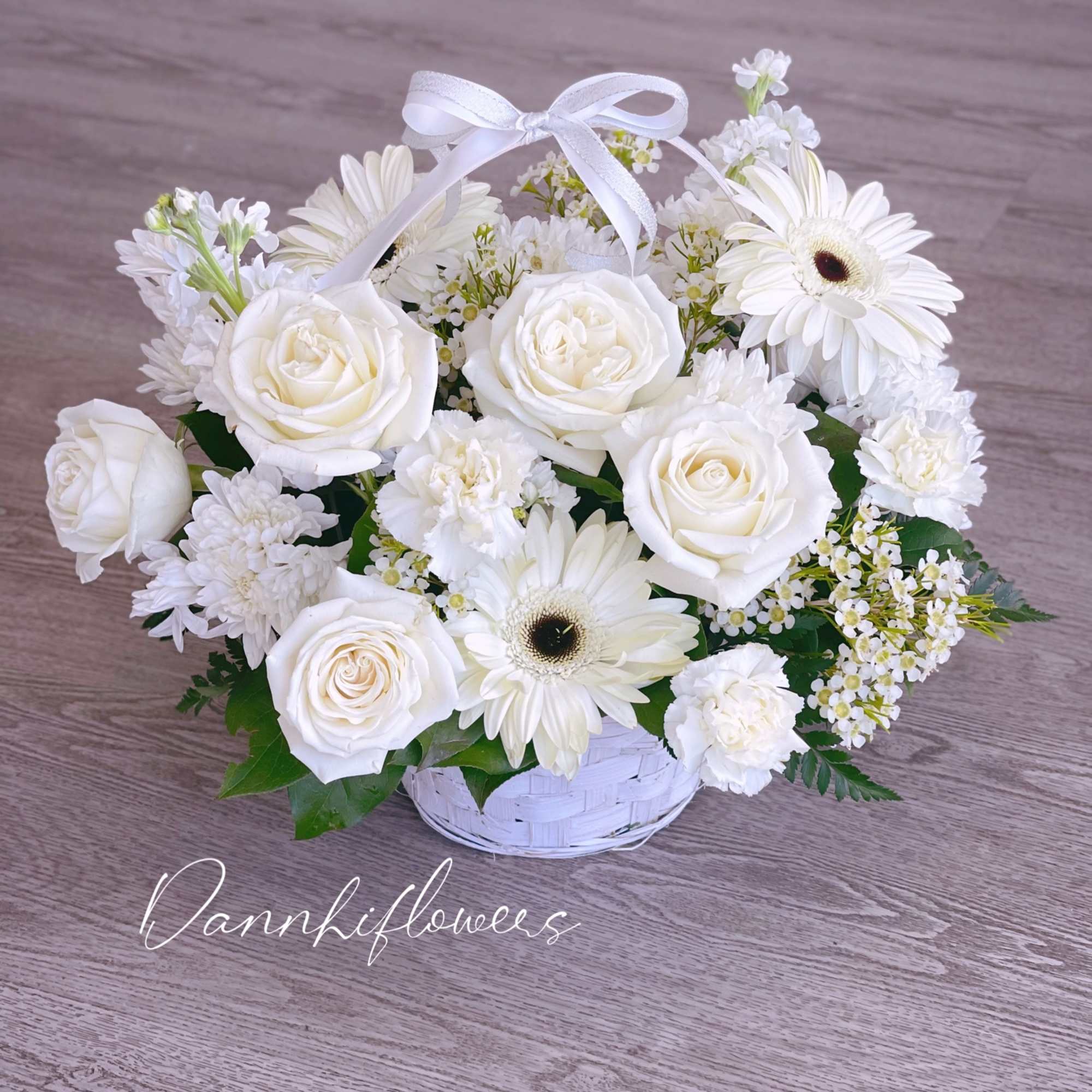 White roses and daisies arranged in a white basket with a ribbon bow