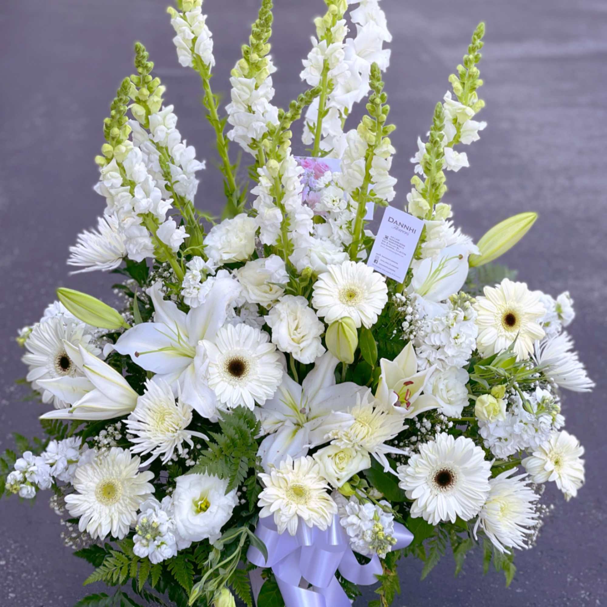 White floral arrangement with lilies, gerbera daisies, and tall snapdragons